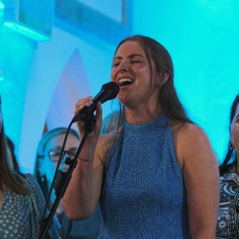 Woman singing into a microphone at a social gathering.