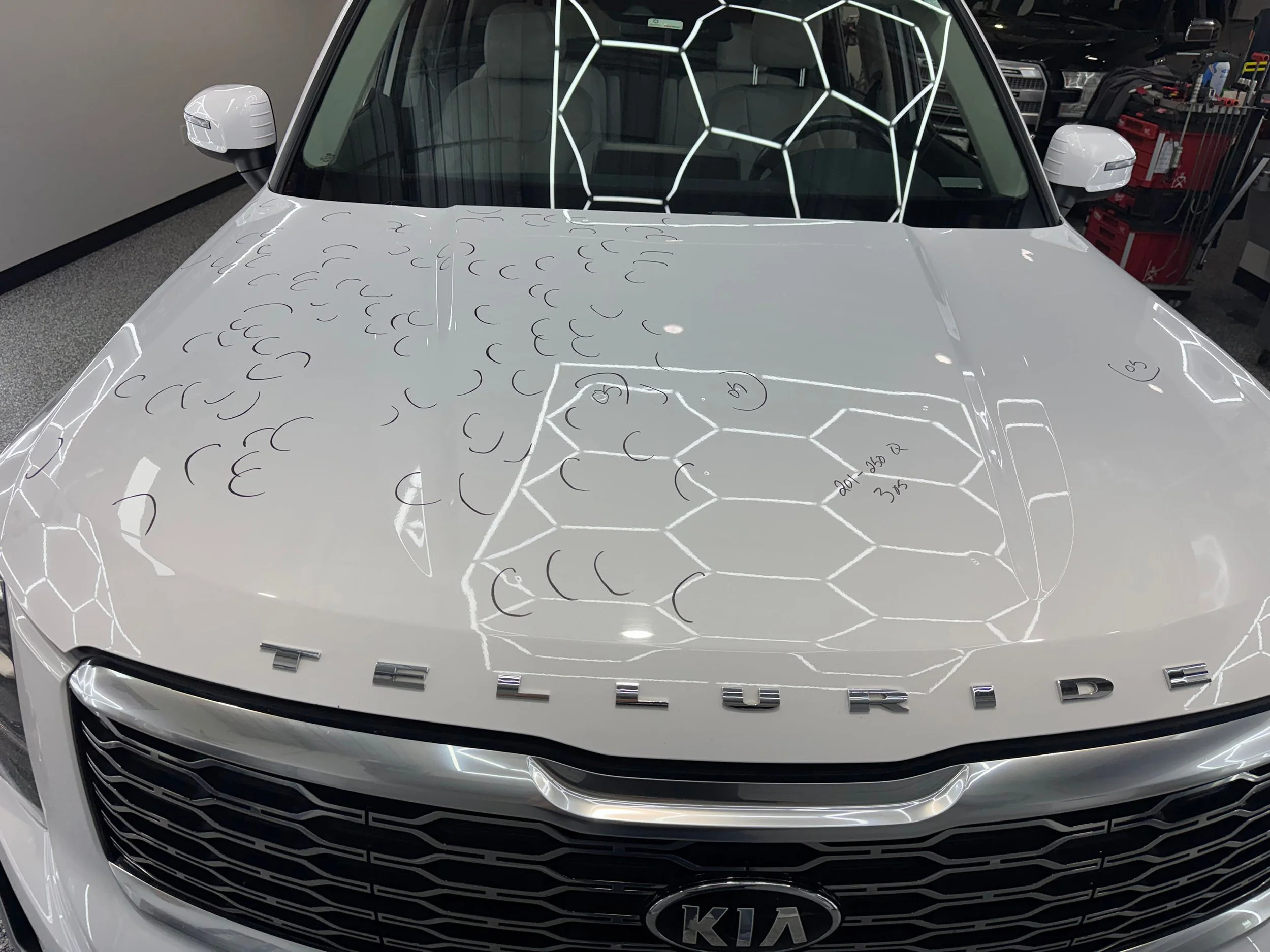 Front view of a white Kia EV6 electric vehicle with dent markings, parked in an indoor garage.