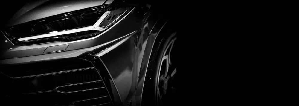 Close-up of the front section of a sleek, modern luxury car, focusing on the headlight and front wheel.