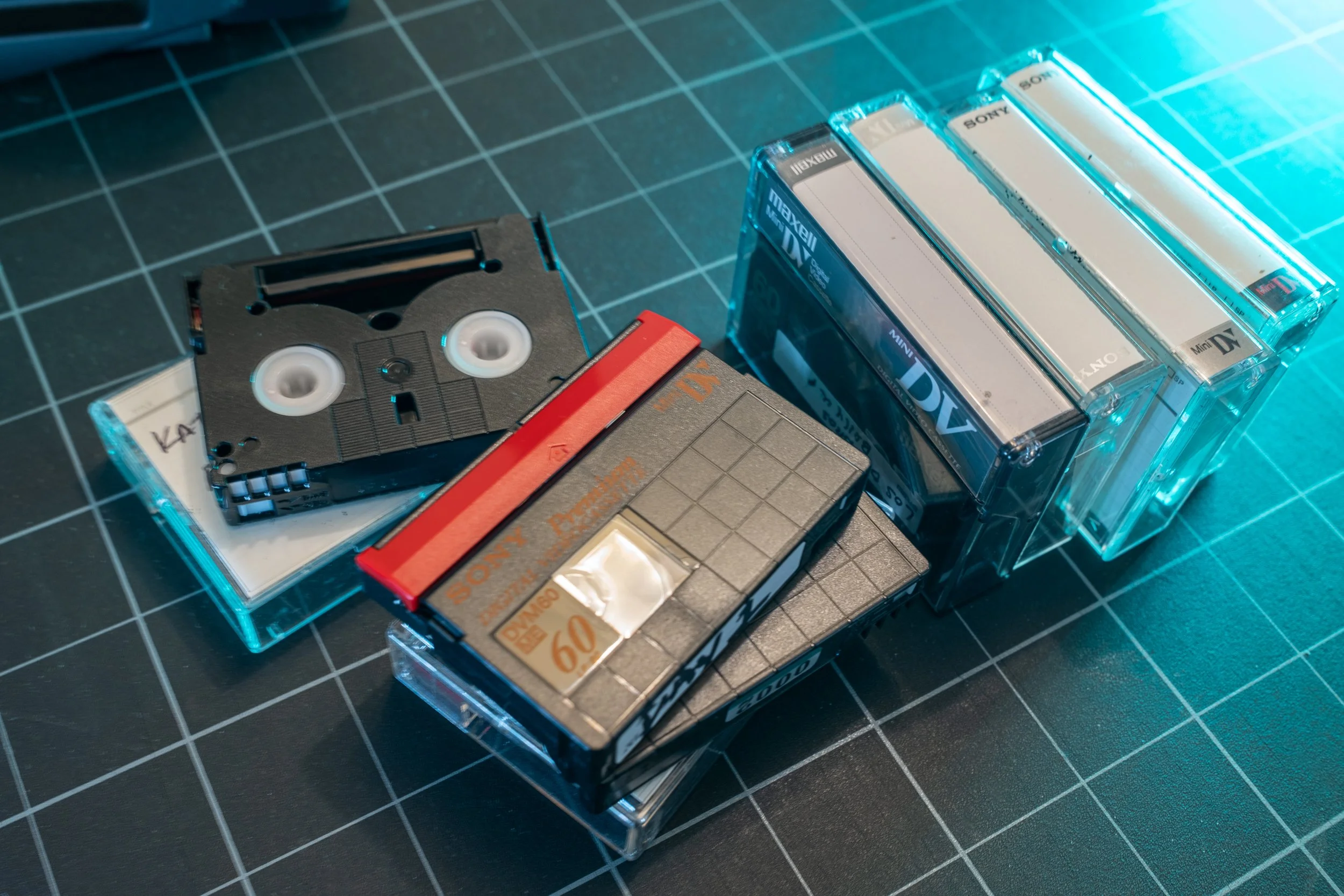 Close-up view of vintage Sony cassette tapes, some in clear plastic cases, placed on a cutting mat with grid lines.