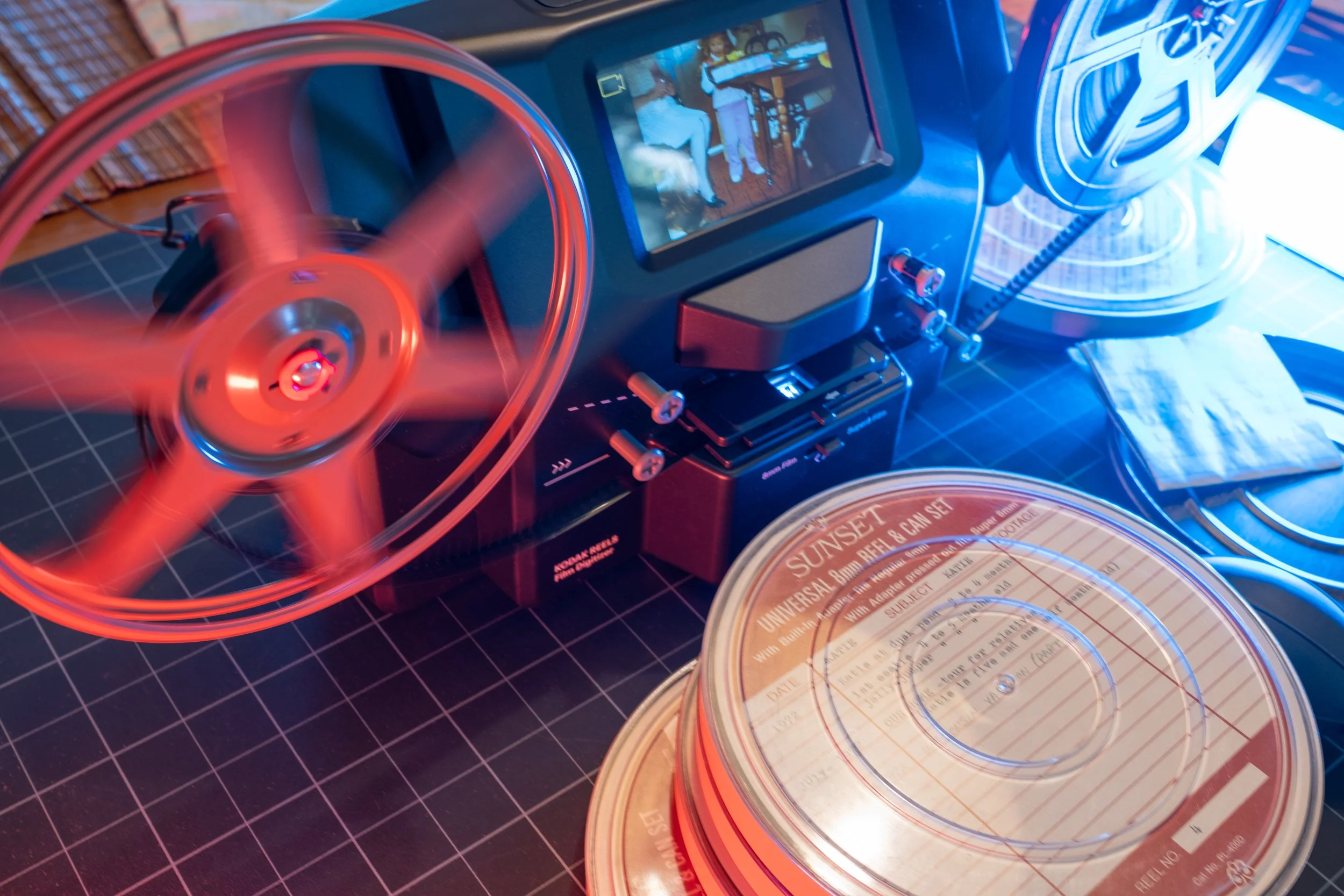 Close-up of a record player with a red spinning record, a tablet displaying an image, and vintage-style paper records with a grid cutting mat underneath.