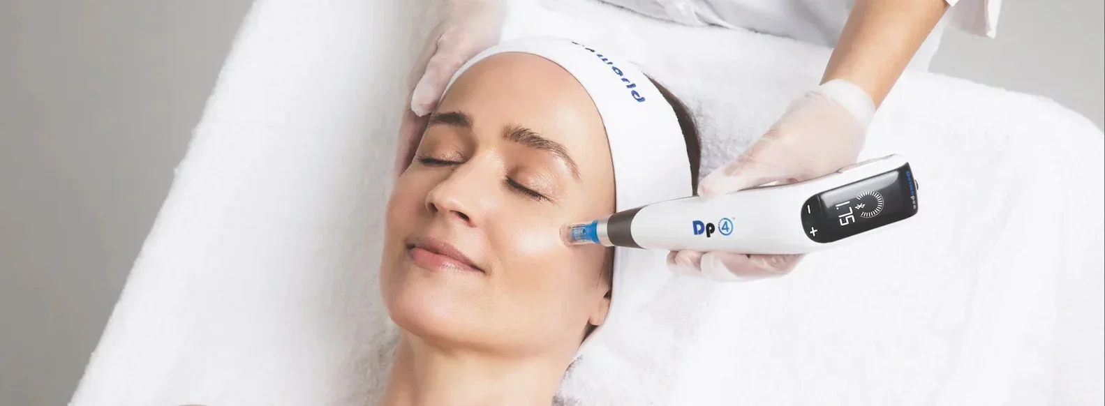 A woman receiving a facial treatment with a device applied to her cheek in a spa setting.