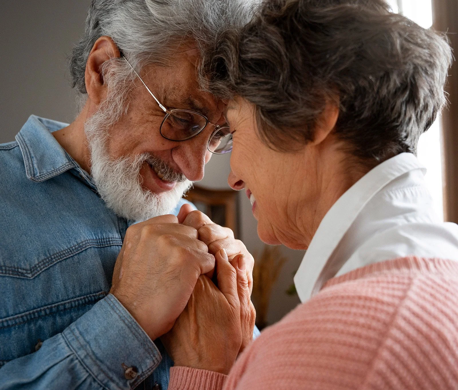 Elderly couple holding hands and touching foreheads, smiling