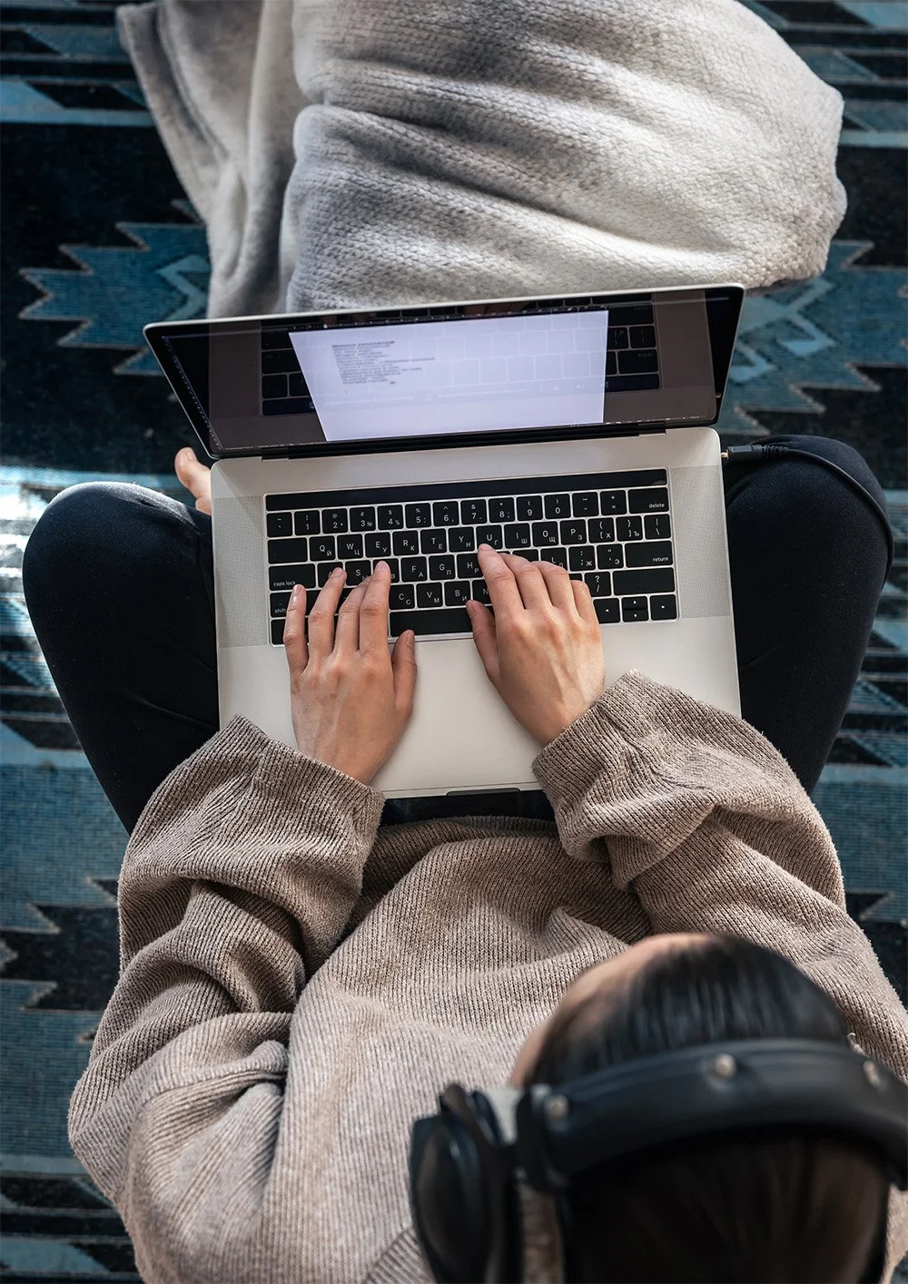 Woman sitting on bed, typing on laptop.