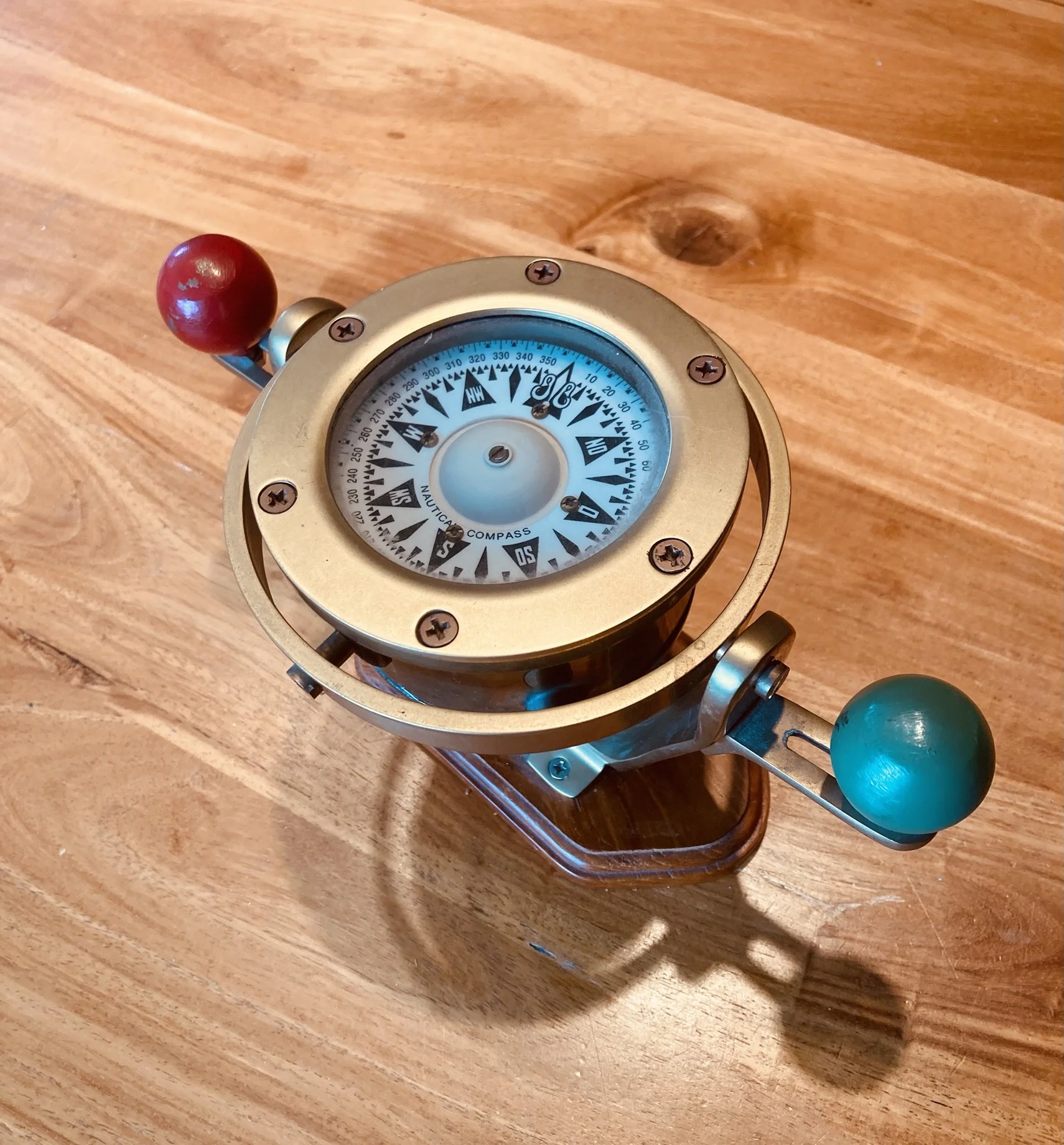 Une boussole nautique avec deux boules colorées, l'une rouge et l'autre turquoise, posée sur une surface en bois.