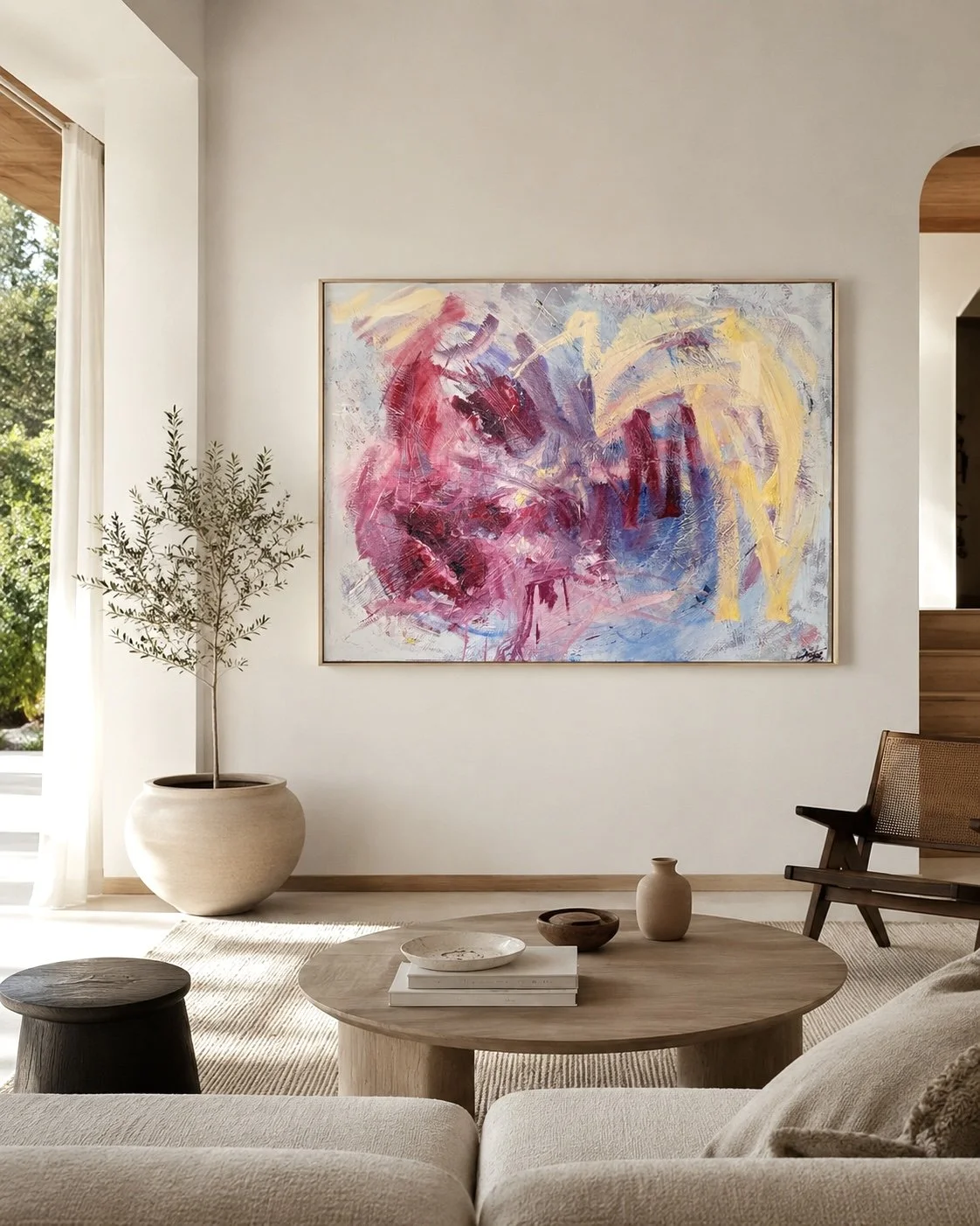 Sunlit modern living room with colorful abstract artwork, potted olive tree, round wood coffee table, and lounge chair