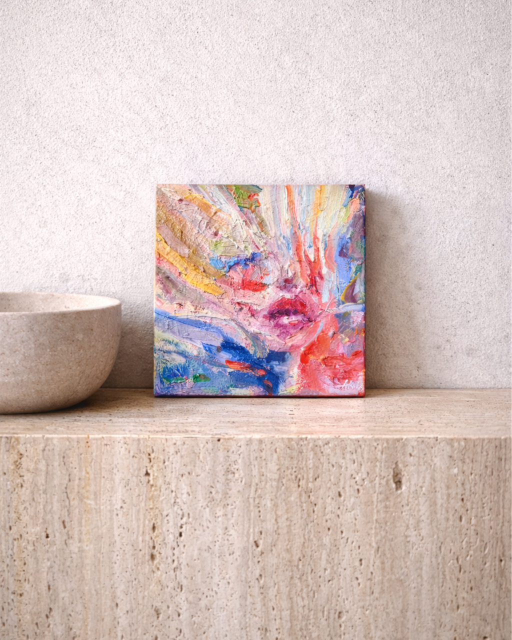 Colorful abstract textured painting displayed on a stone shelf beside a ceramic bowl