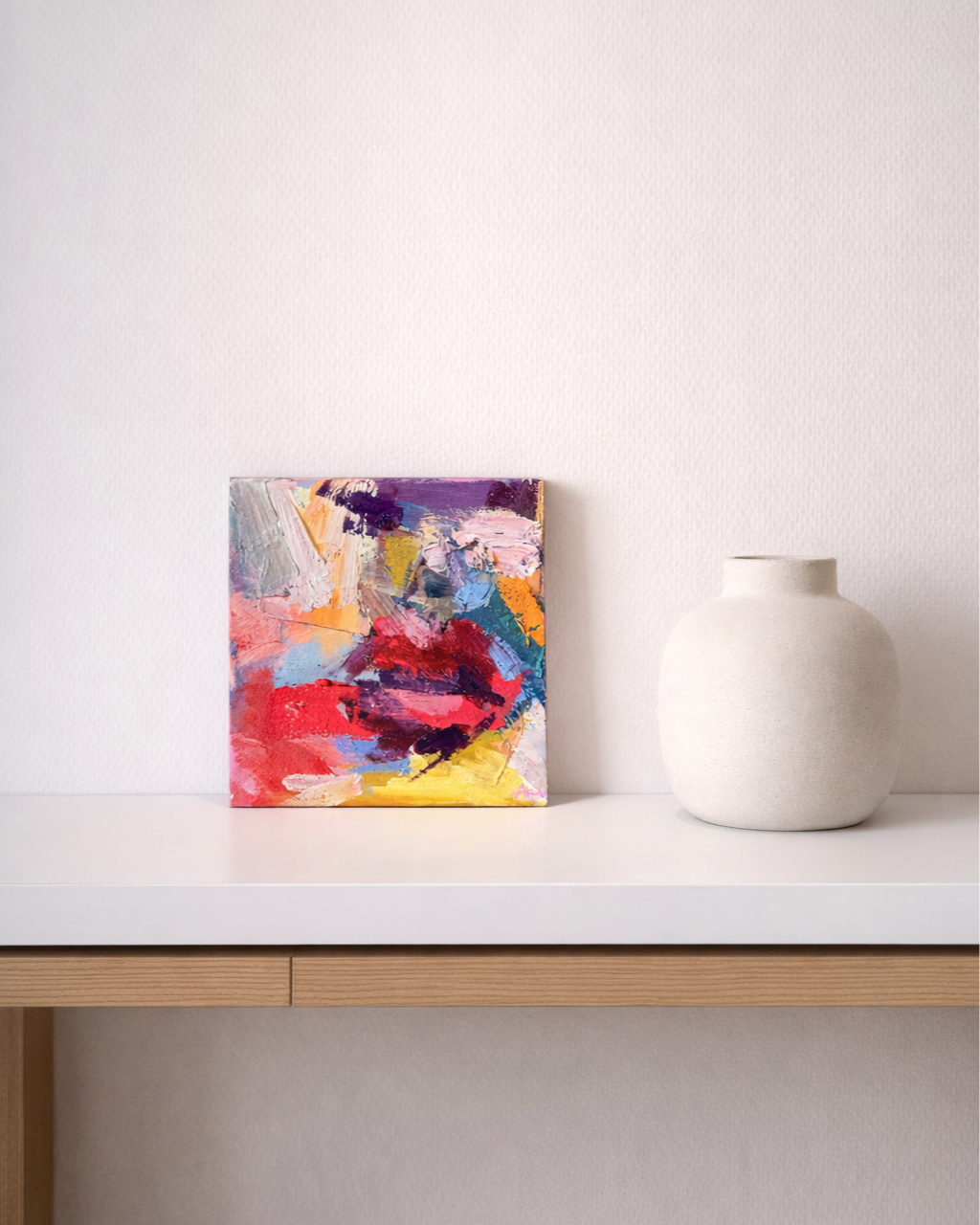 Colorful abstract painting and white ceramic vase displayed on a modern wooden console table