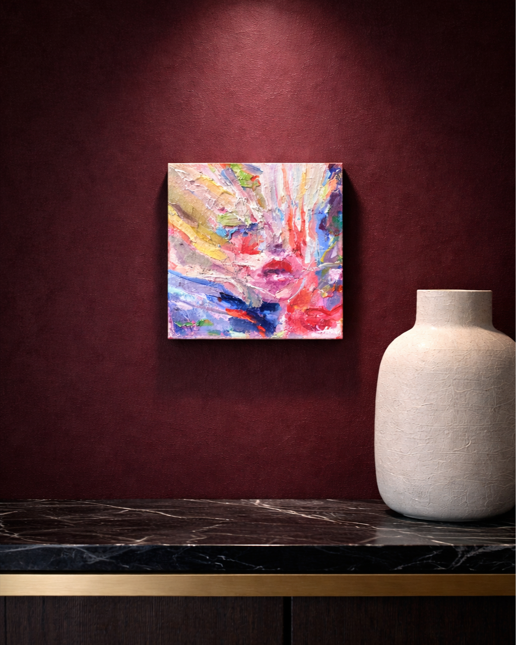 Colorful abstract painting and white textured ceramic vase displayed against a burgundy wall on a dark marble console table