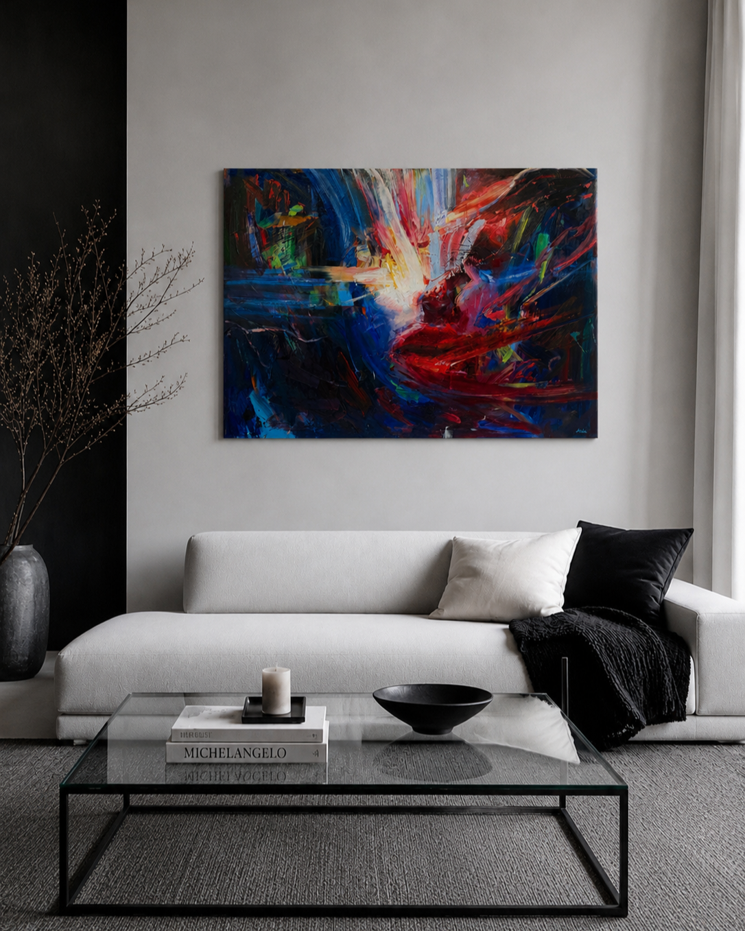 Modern living room with a white sectional sofa, colorful abstract painting, glass coffee table, black bowl, candle, and stacked art books.