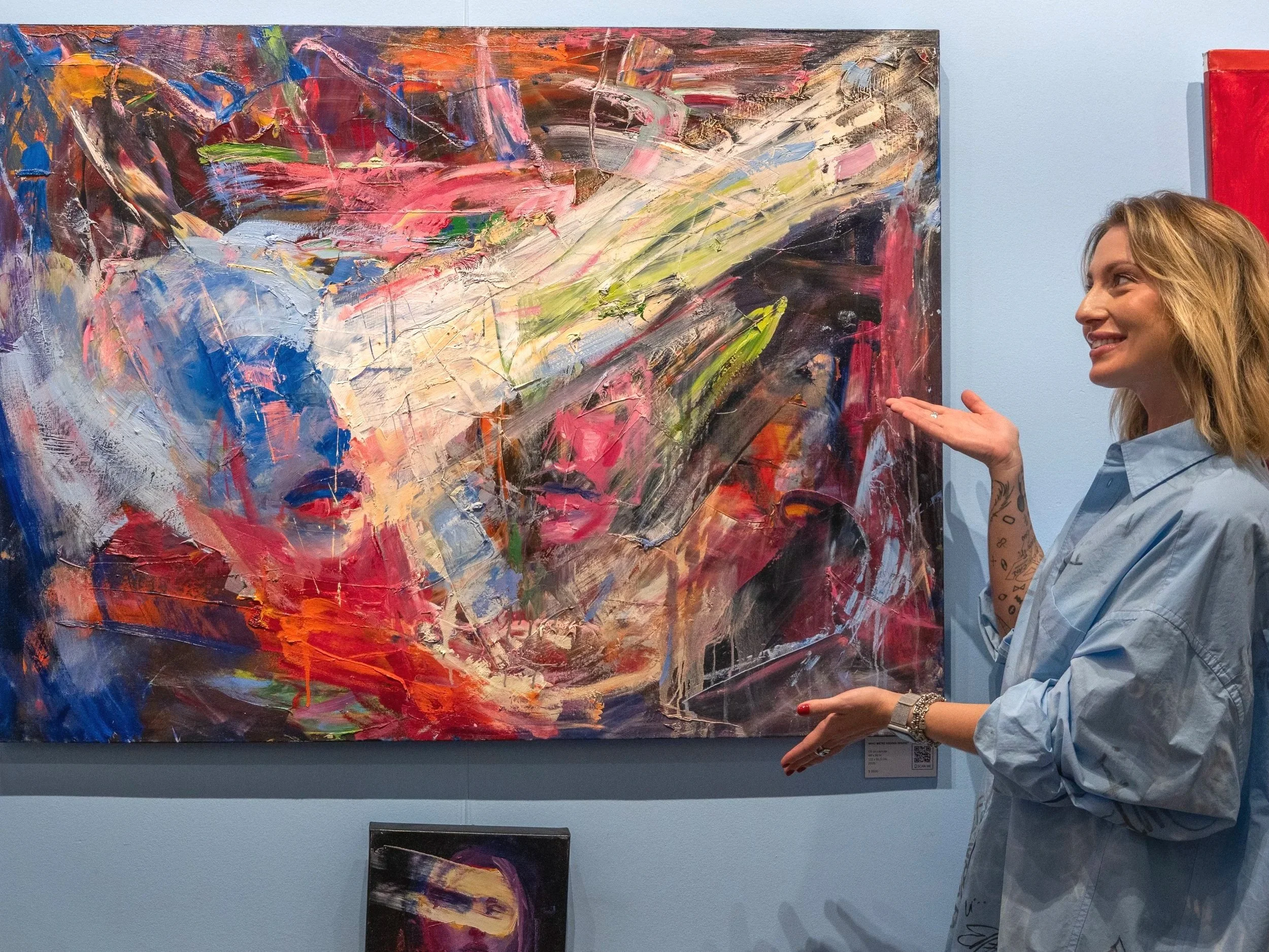 Woman presenting a large, colorful abstract painting in an art gallery
