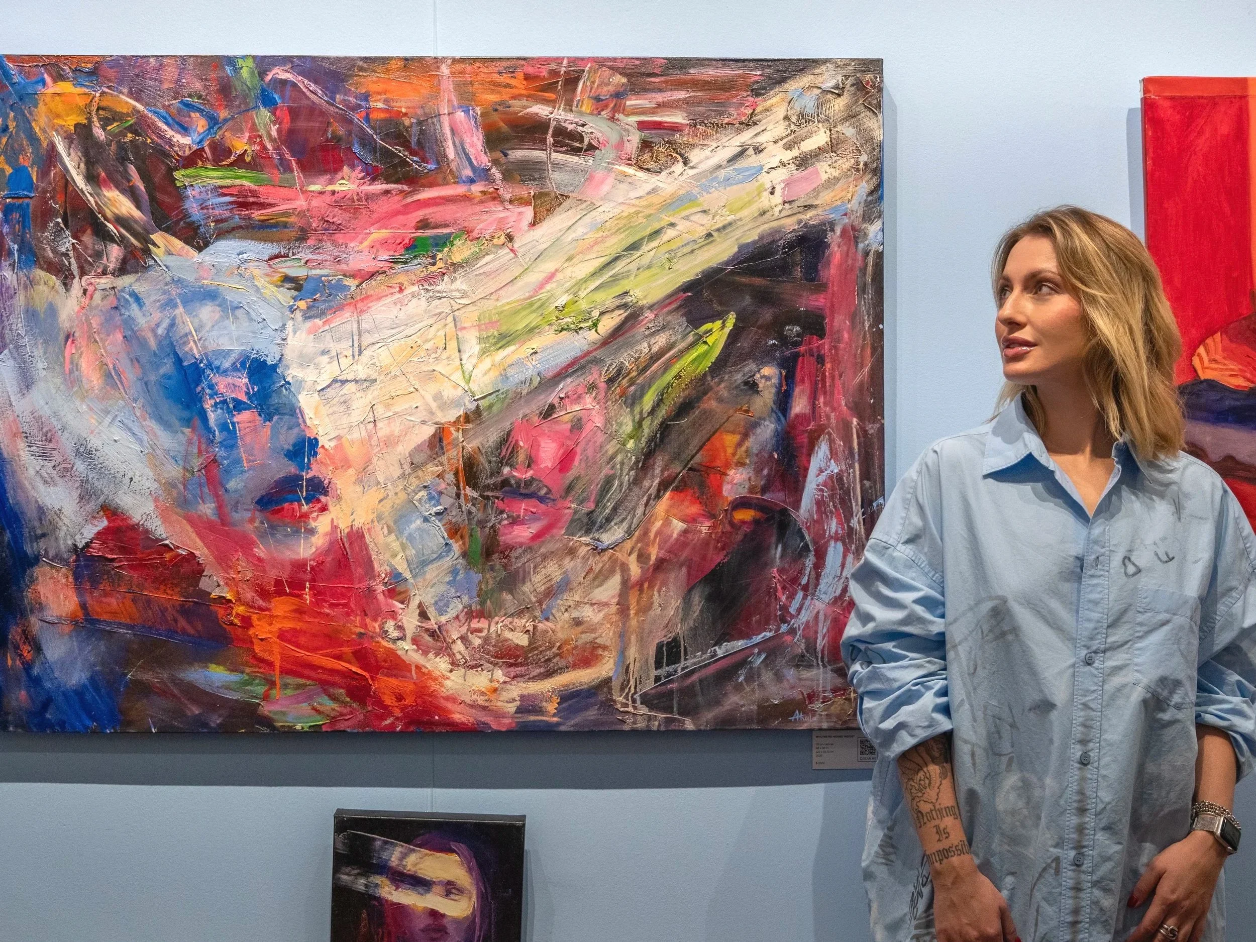 Woman standing beside a large colorful abstract painting in an art gallery