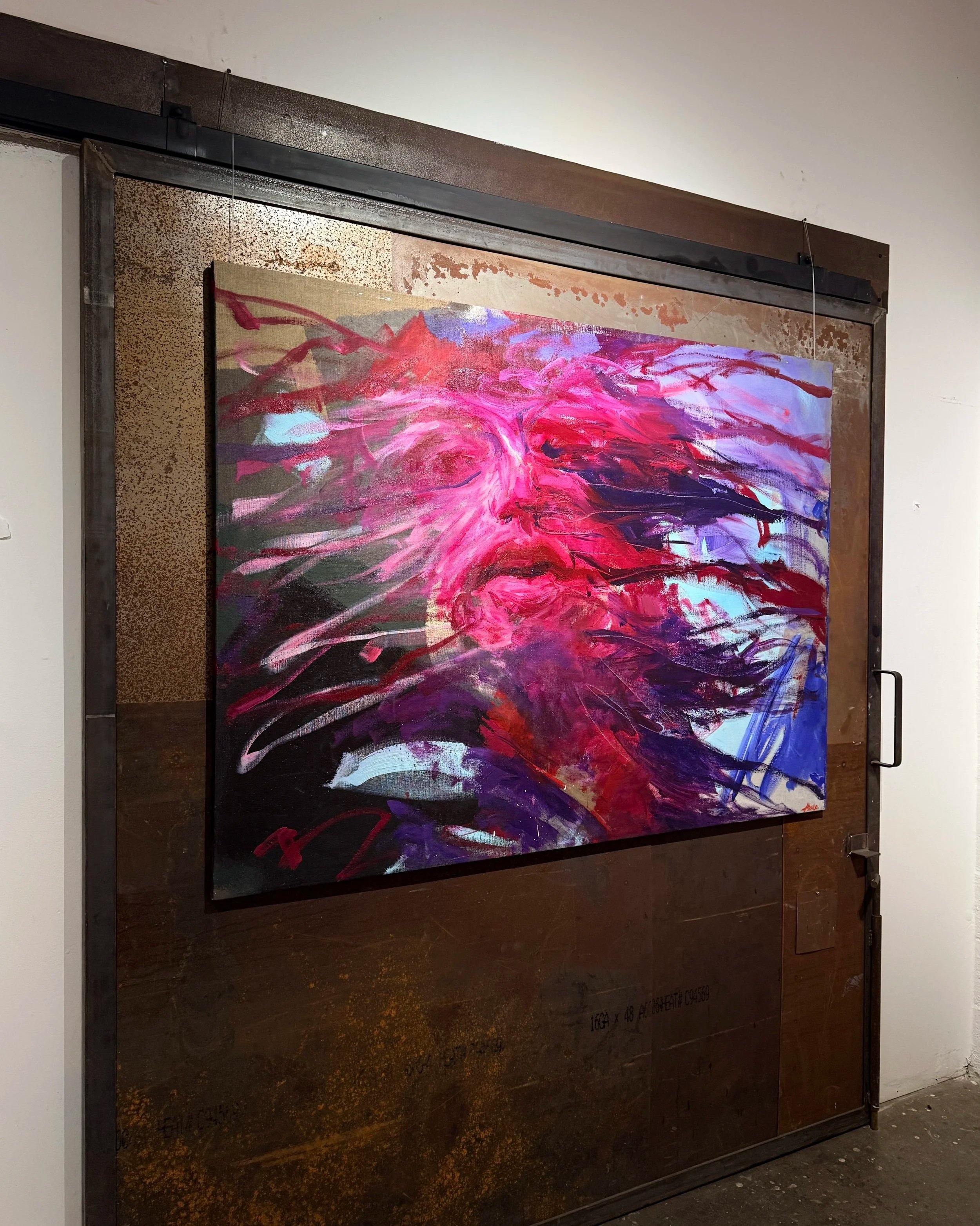 Vibrant abstract painting in pink, purple, red, blue, and black displayed on a rustic metal industrial door.