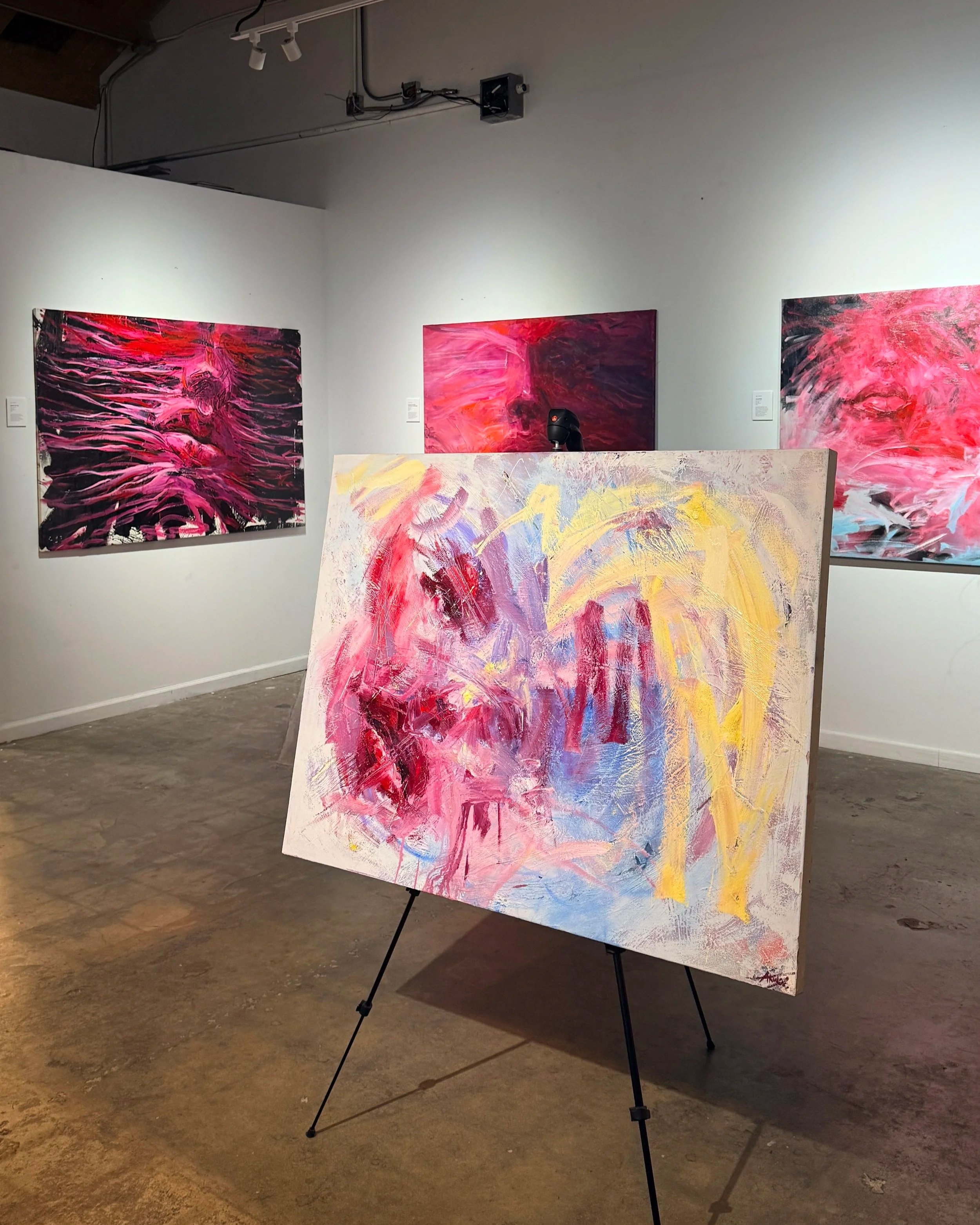 Abstract art gallery displaying vibrant pink, red, purple, yellow, and blue paintings on walls and an easel.