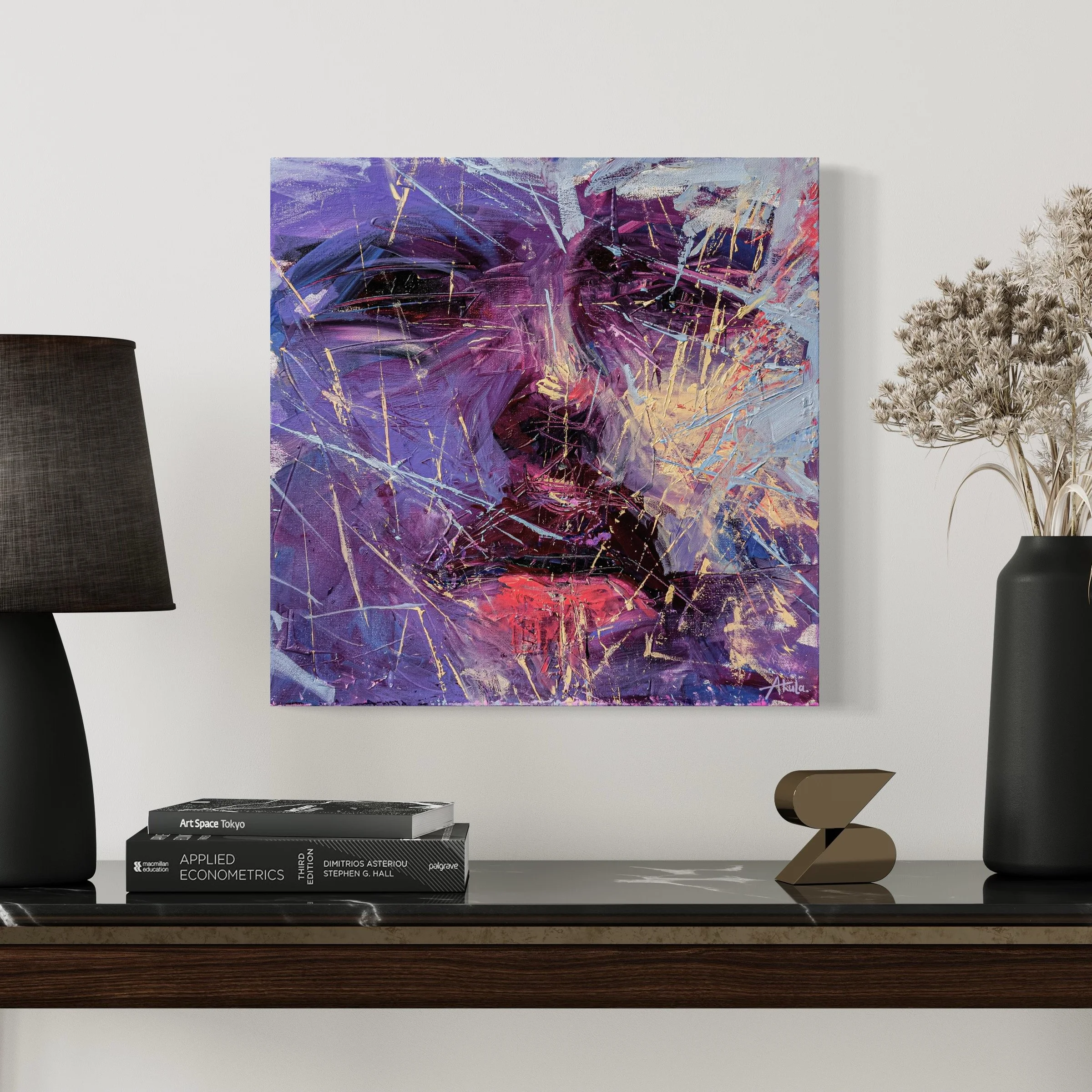 Abstract purple, blue, and gold painting displayed above a console table with books, lamps, a sculpture, and a vase of dried flowers