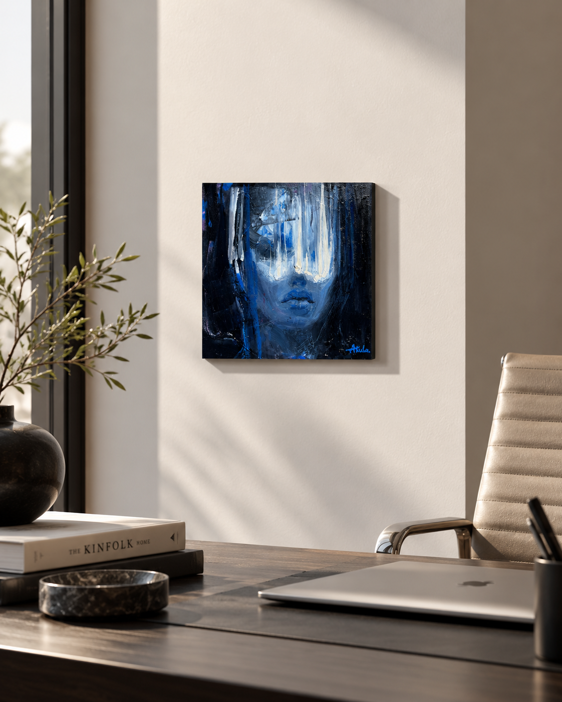 Modern home office with blue abstract portrait painting, wooden desk, laptop, black vase, books, and leather chair