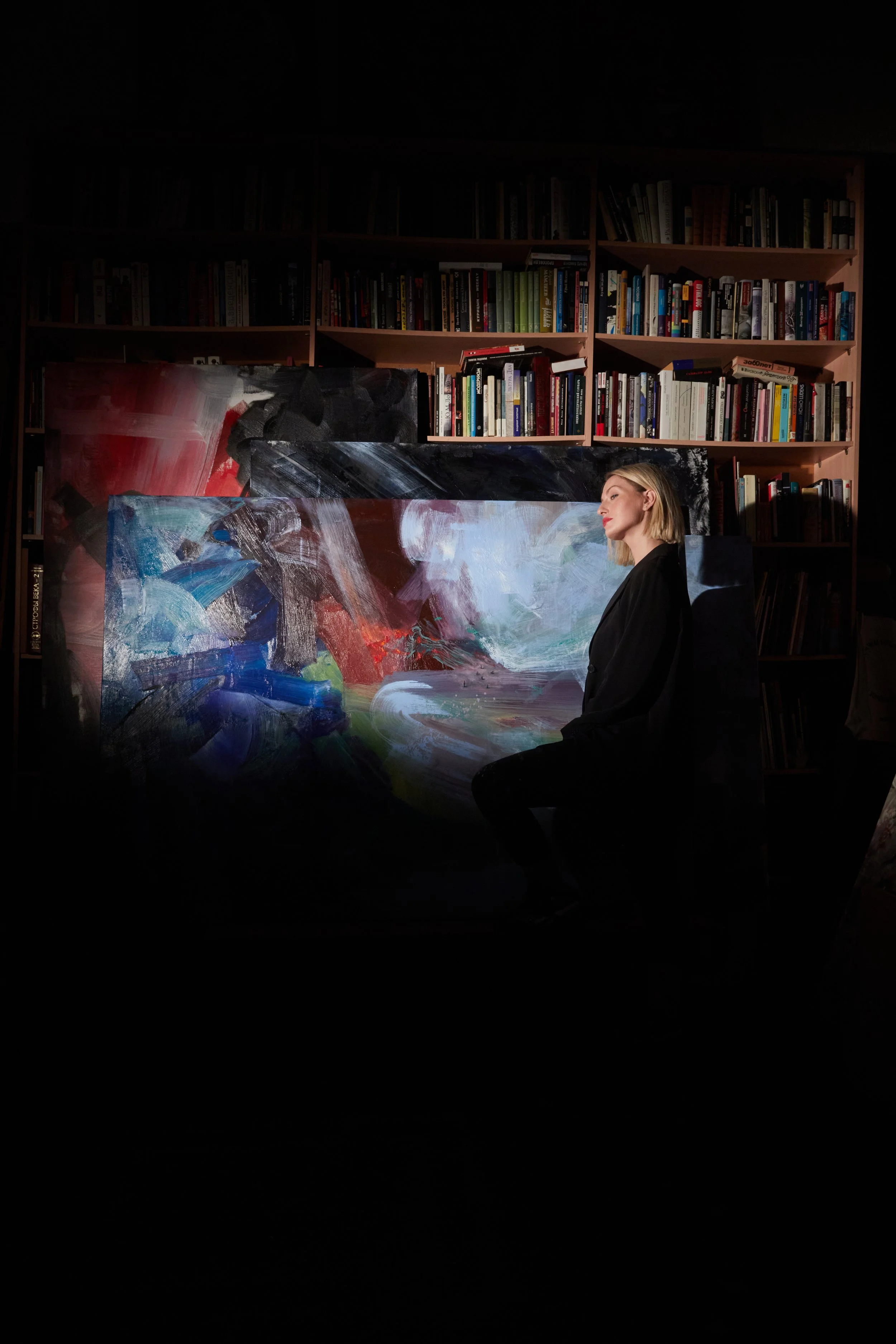 Woman in black standing beside a large abstract painting in front of bookshelves filled with books