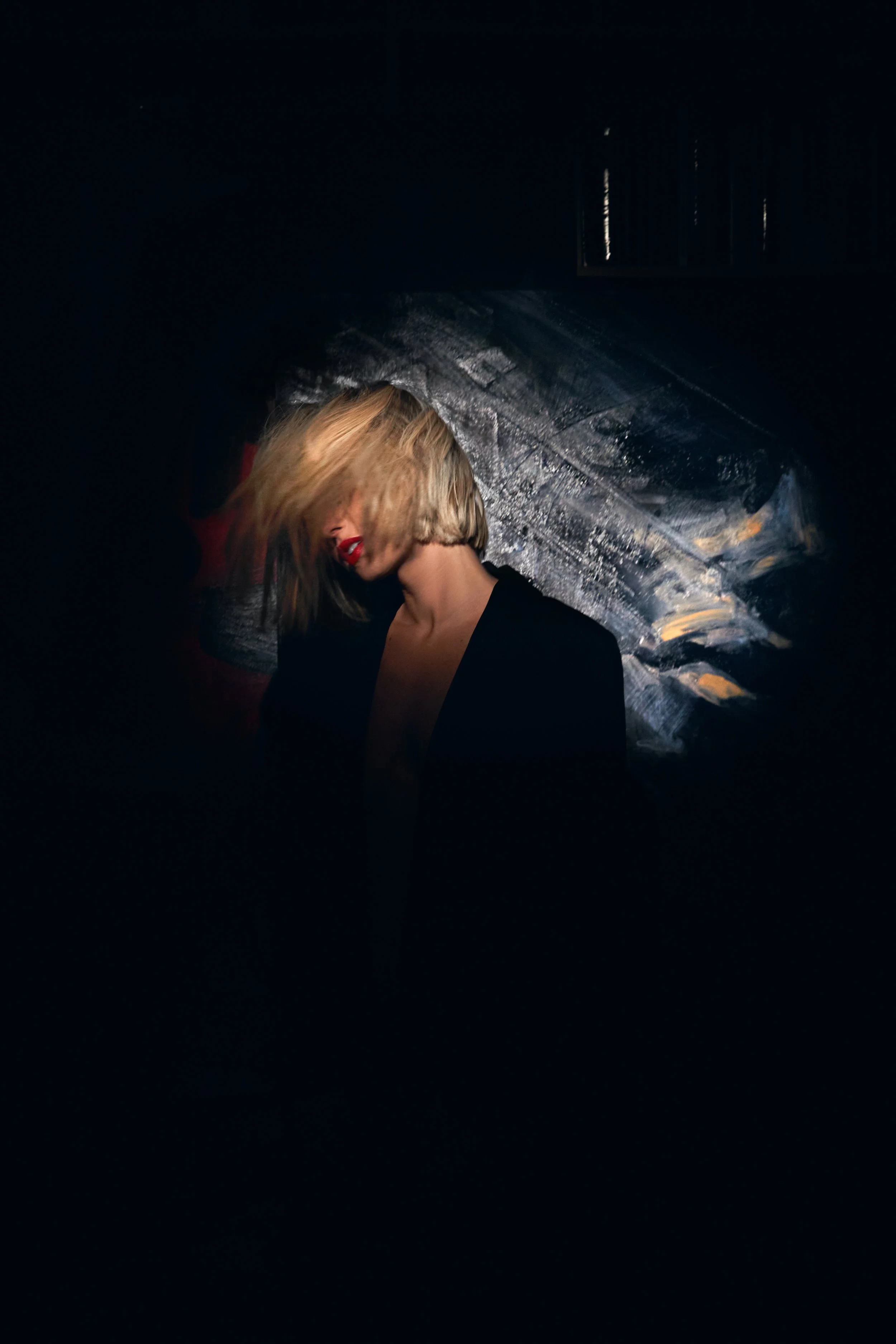 Blonde woman with red lipstick wearing a black outfit in front of a dark, glittering backdrop