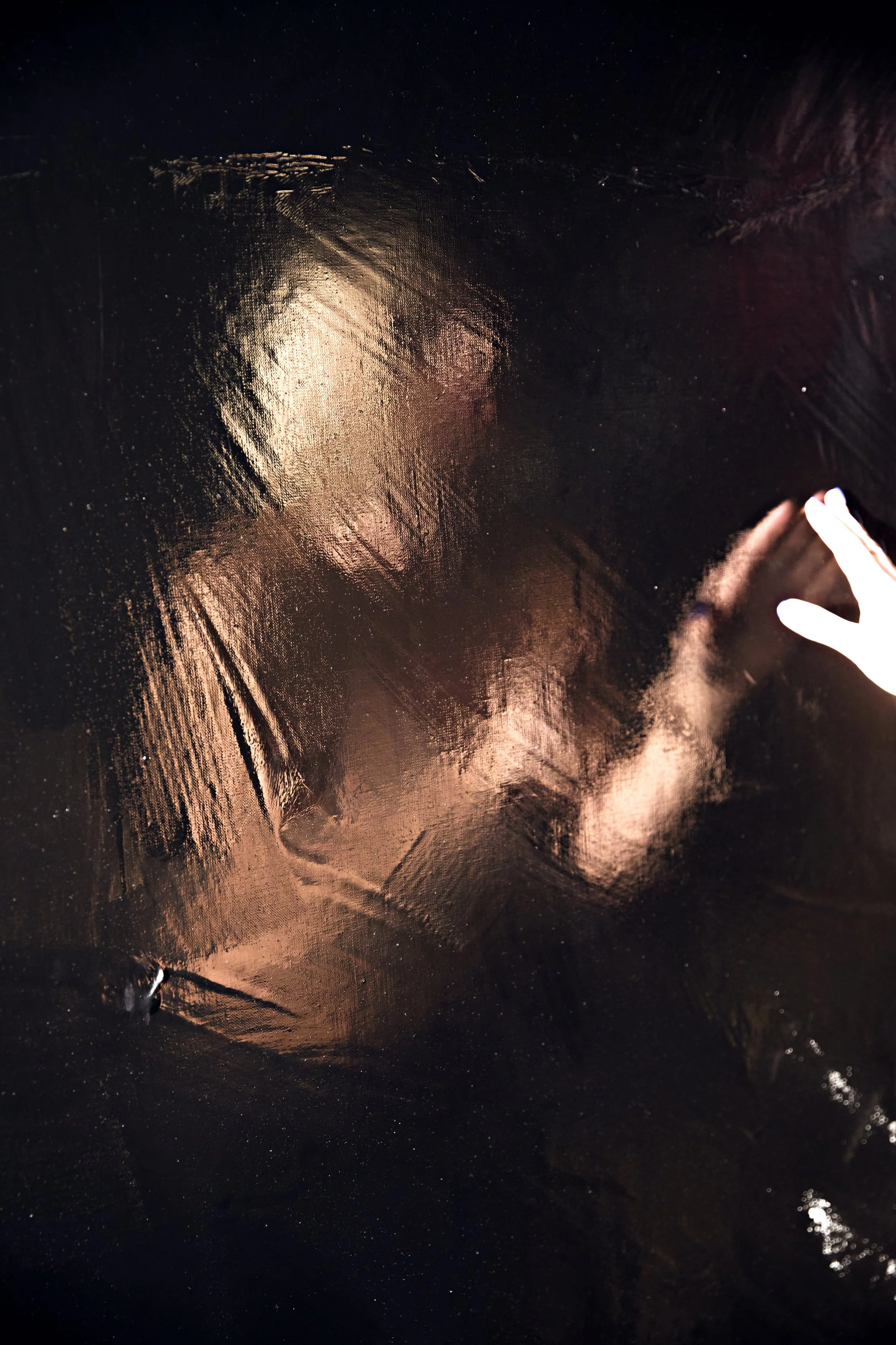 Close-up of a black textured fabric with dramatic light reflections and a hand partially visible at the lower right.
