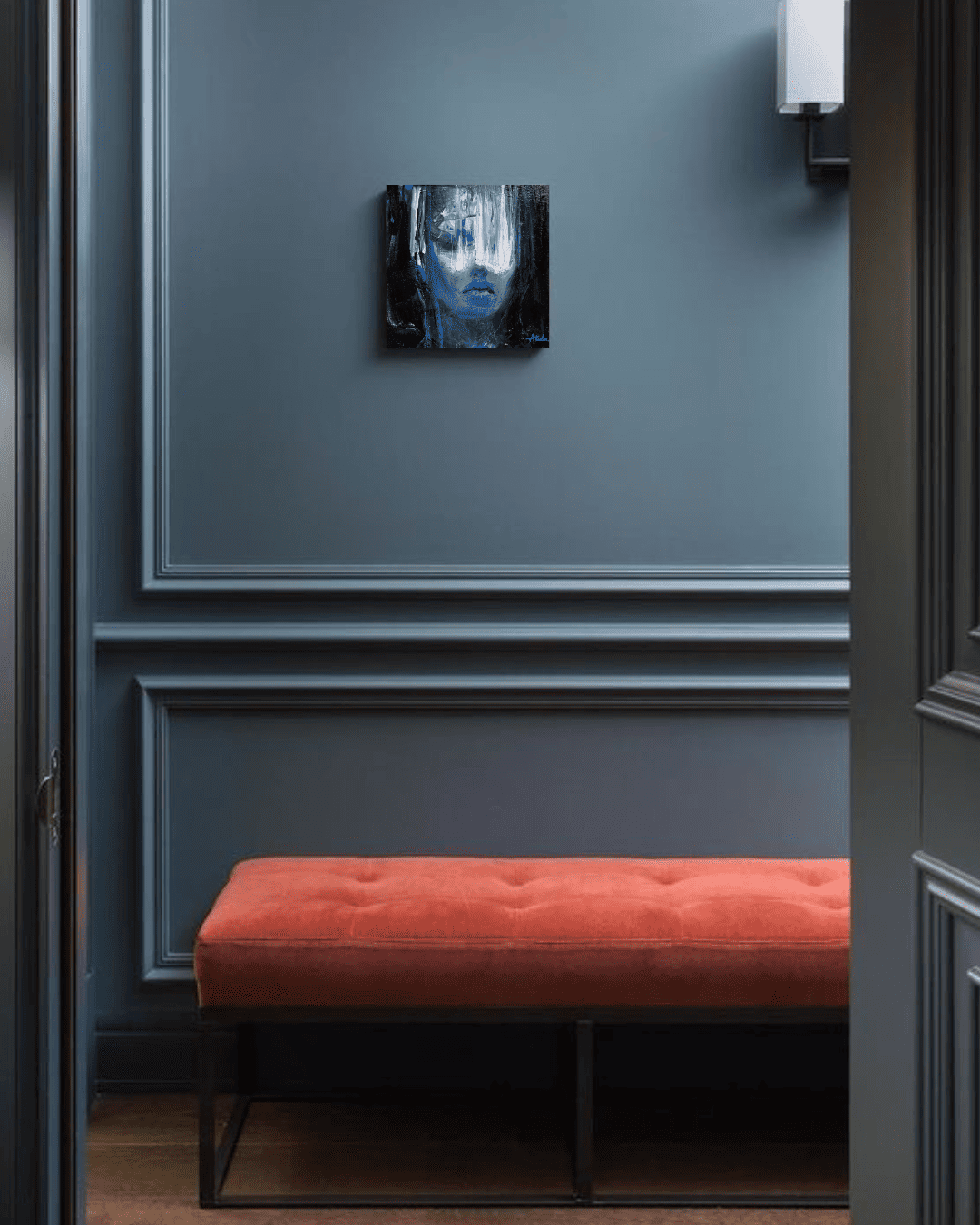 Red tufted bench beneath abstract blue portrait in a dark blue paneled room