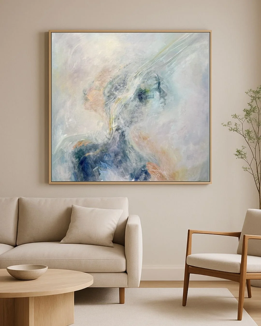 Abstract pastel painting above a beige sofa in a minimalist living room with a wood coffee table, armchair, and tall plant