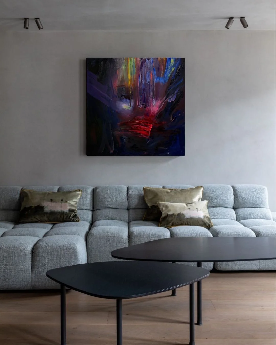 Modern living room with a gray sectional sofa, black nesting coffee tables, colorful abstract painting, and decorative pillows