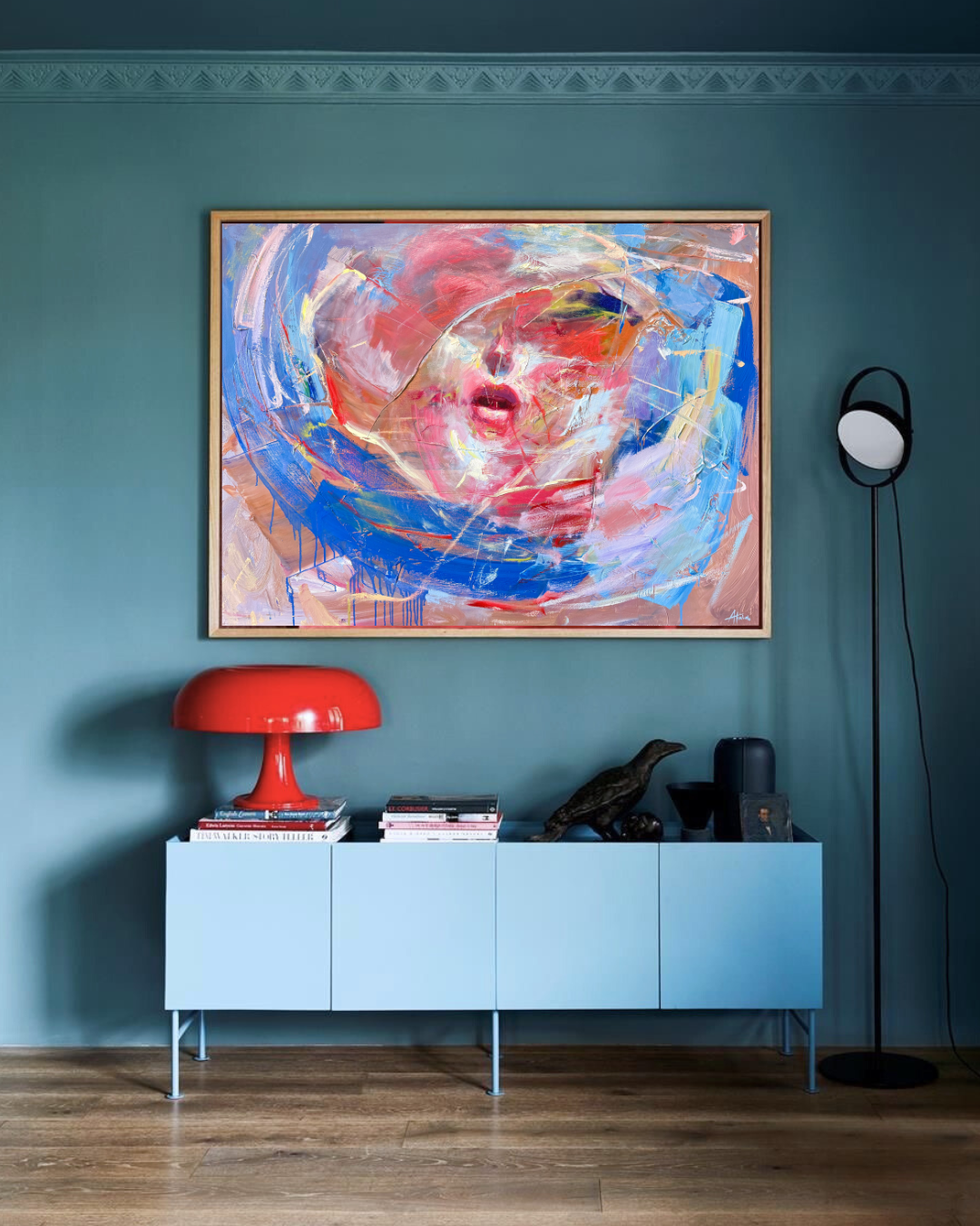Stylish teal living room with colorful abstract portrait painting, red table lamp, blue sideboard, books, and black floor lamp