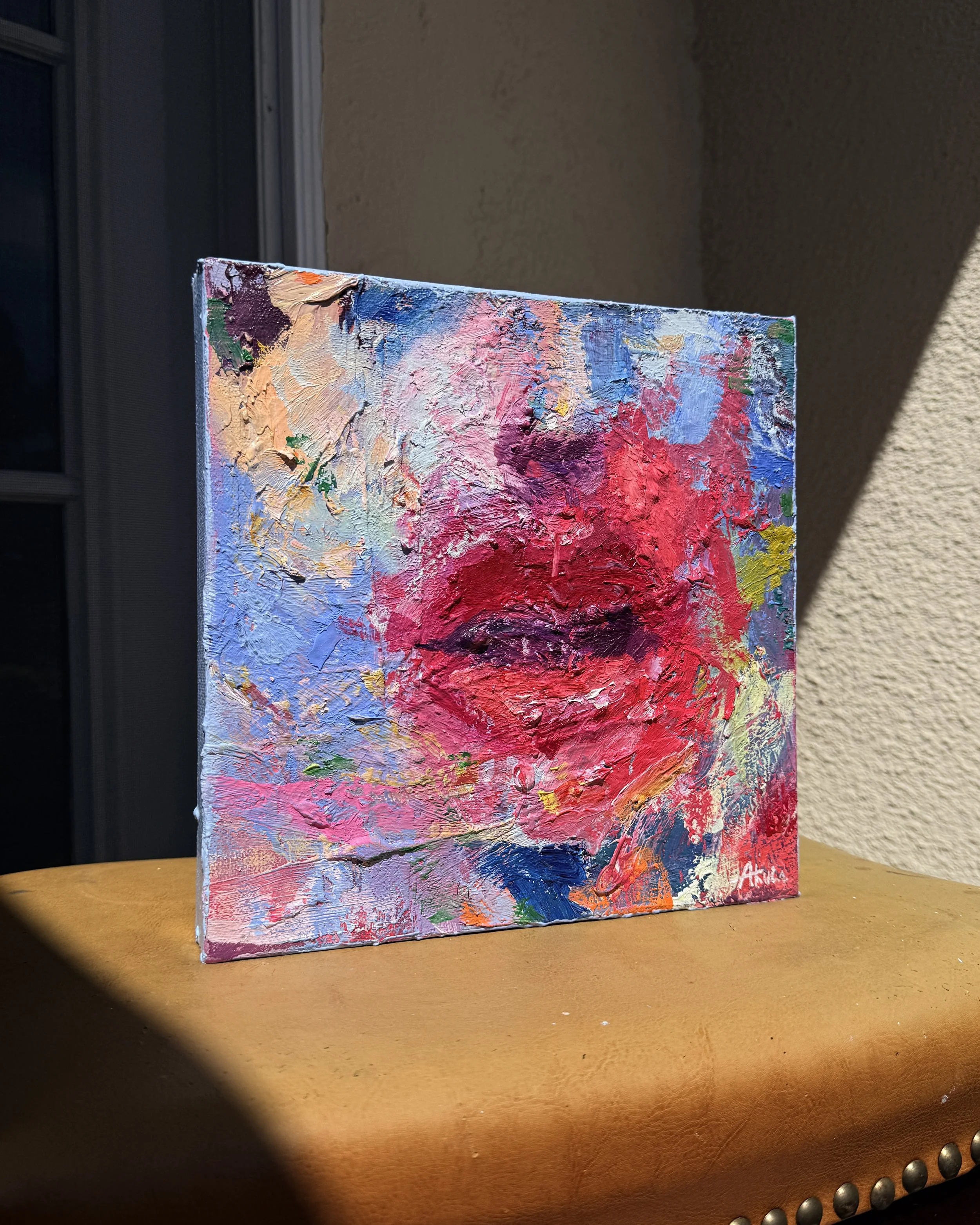 Close-up of a vibrant abstract impasto painting with thick pink, red, blue, purple, and orange brushstrokes on a canvas.