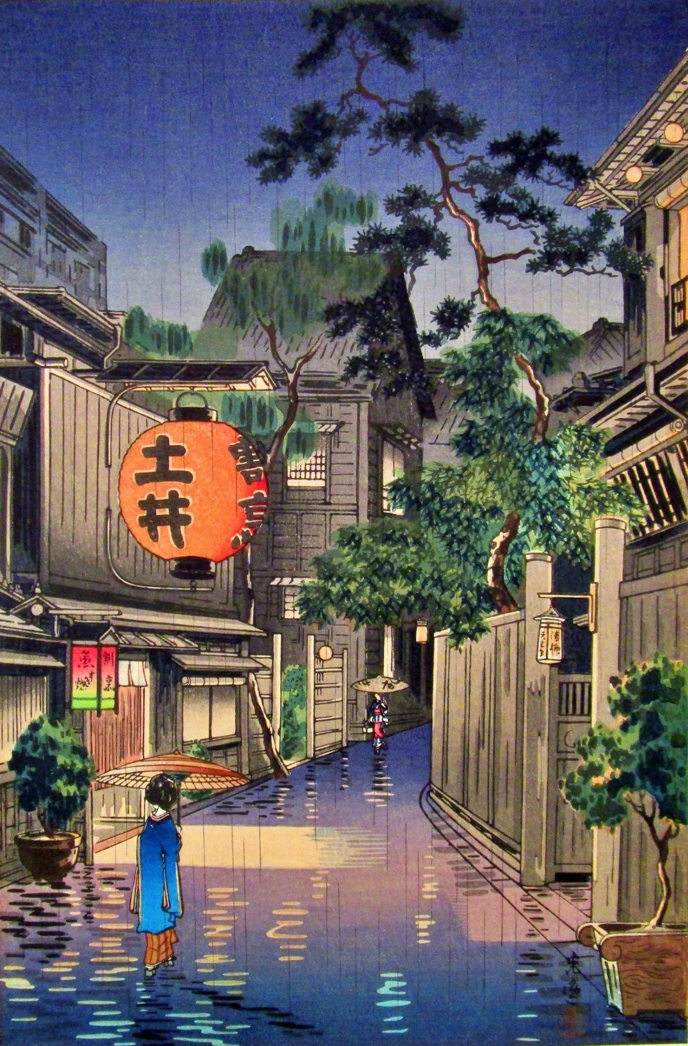 Ushigome Kagurazaka by Tsuchiya Kōitsu: two figures beneath umbrellas on a blue rain-washed lane, a large orange Doi lantern, glowing windows, wooden buildings, a tall pine and lush green foliage.