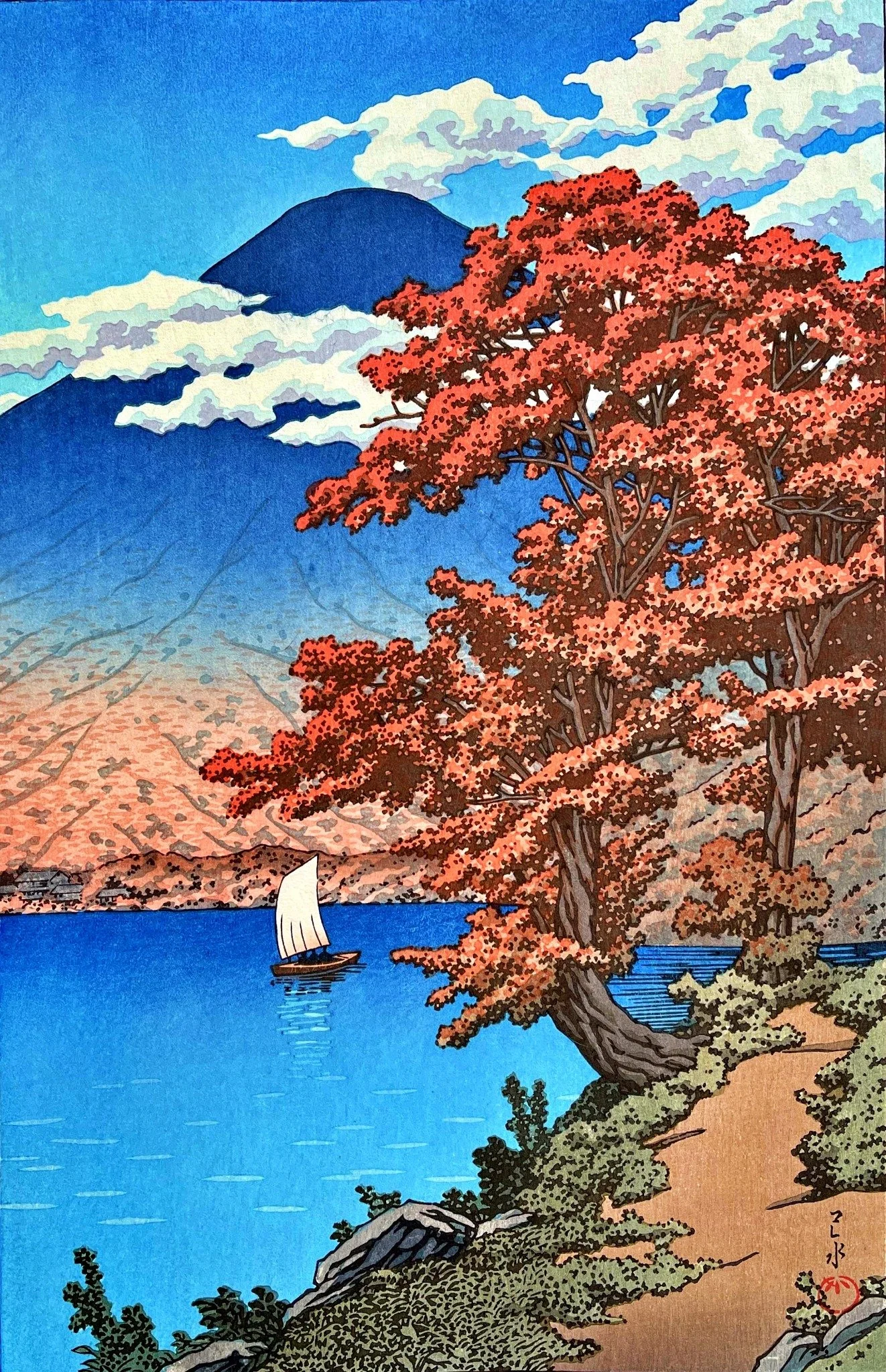 Lake Chūzenji at Nikkō by Kawase Hasui: red autumn trees beside a curving ochre shore, a white sailboat on bright blue water, a large blue mountain and layered pale clouds.