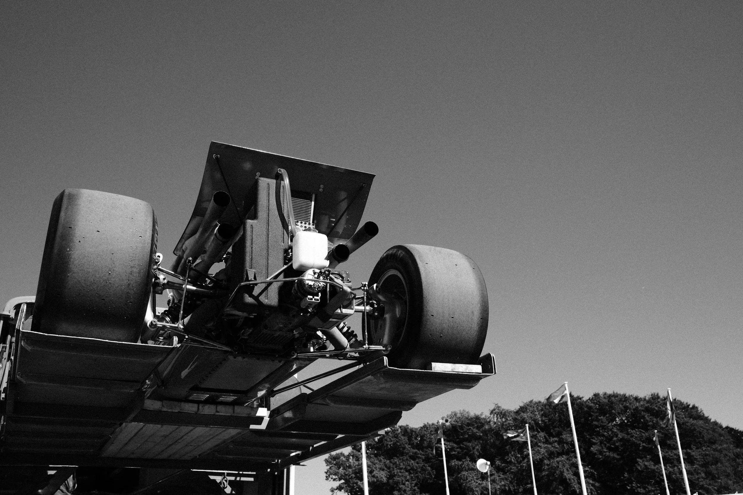 Black-and-white photograph of a vintage Ferrari Formula 1 car being lifted onto a transporter at the Goodwood Festival of Speed.