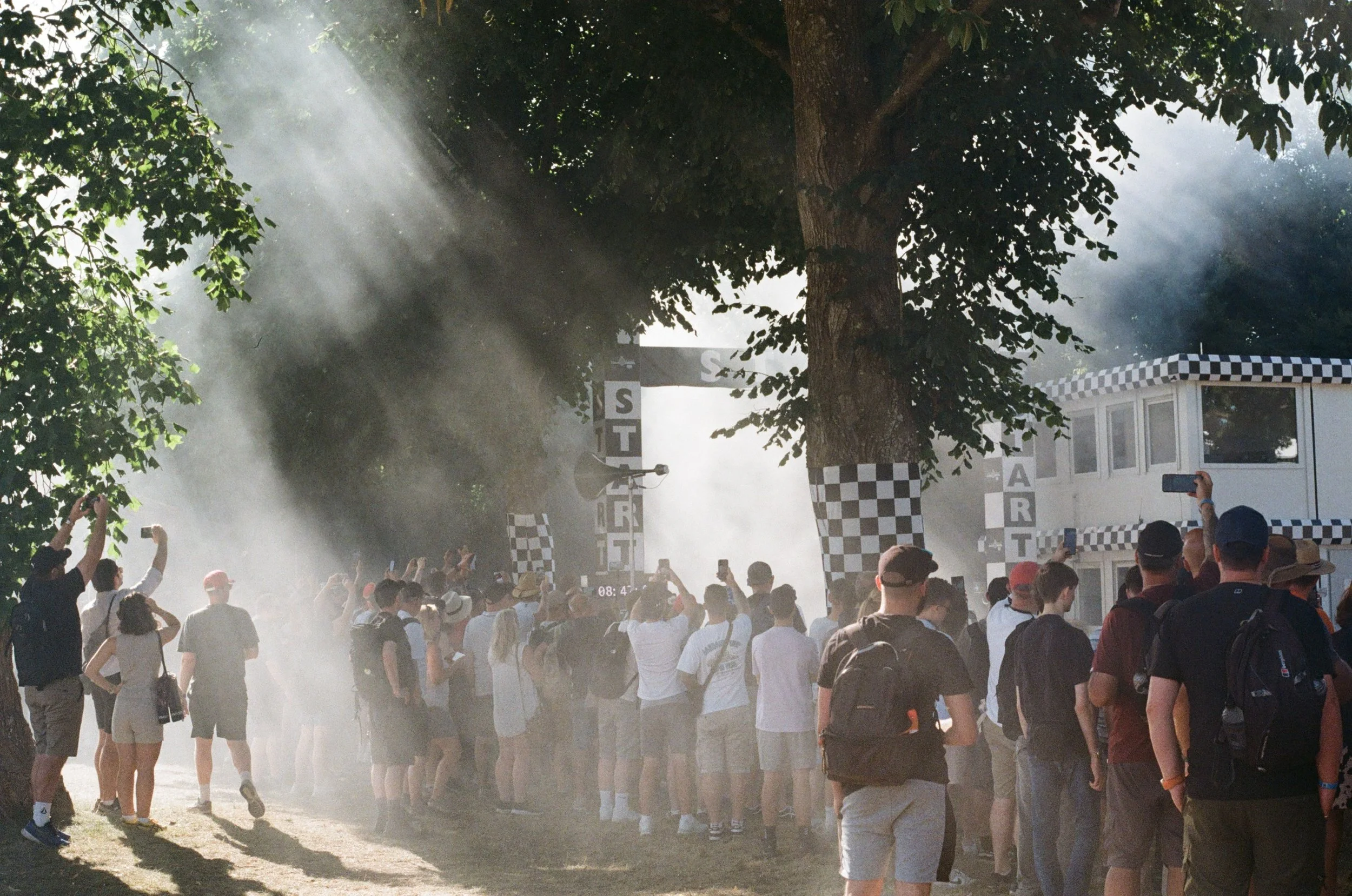 Spectators gathered beside the start line at the Goodwood Festival of Speed as tyre smoke drifts through the crowd and sunlight.