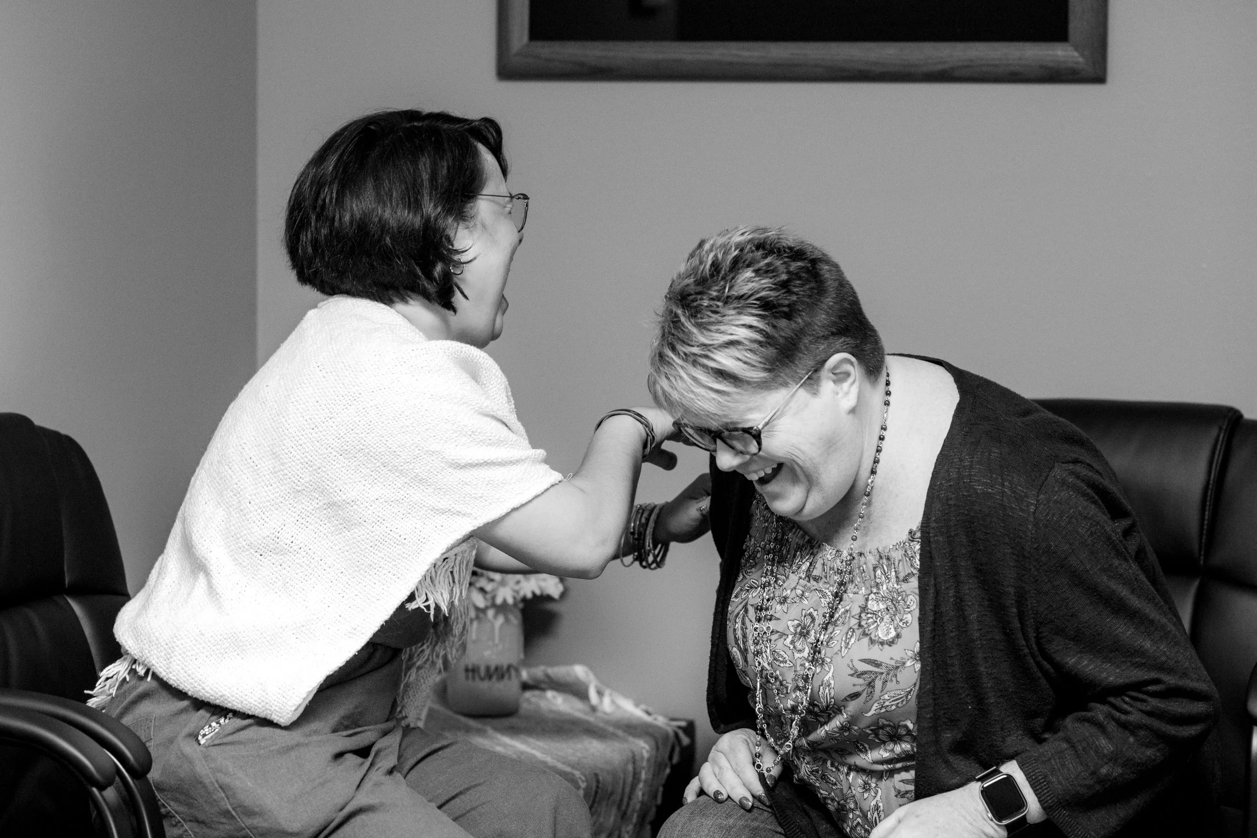 Two women sharing a laugh, one is in a wheelchair and the other is seated, engaged in a joyful moment.