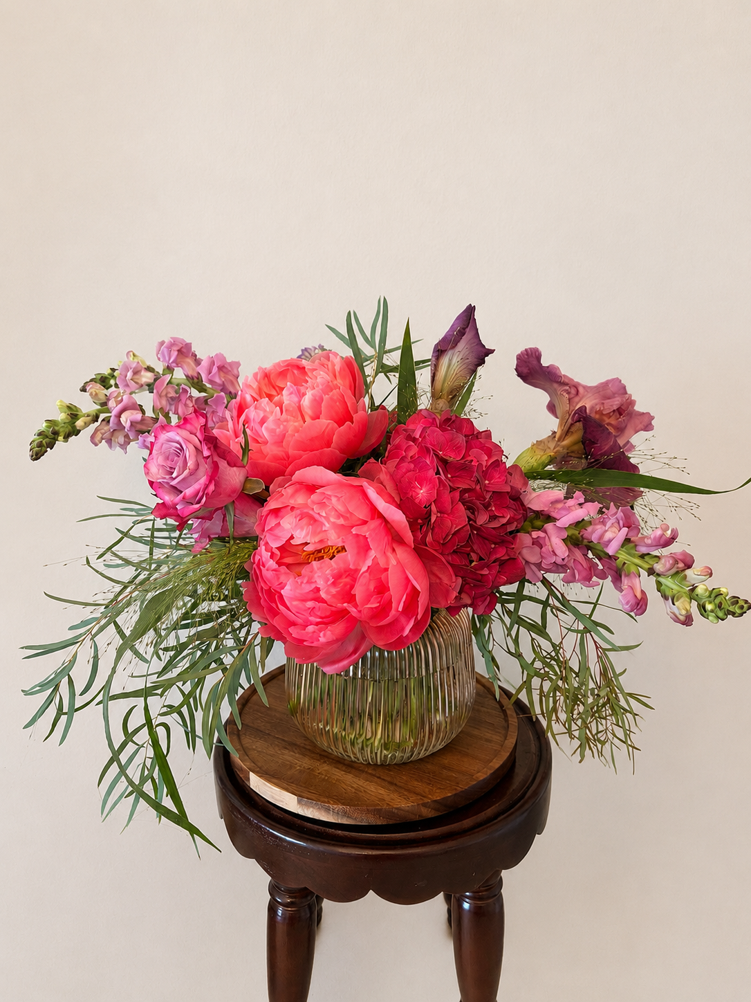 A colorful bouquet of pink, purple, and red flowers in a glass vase on a wooden table.