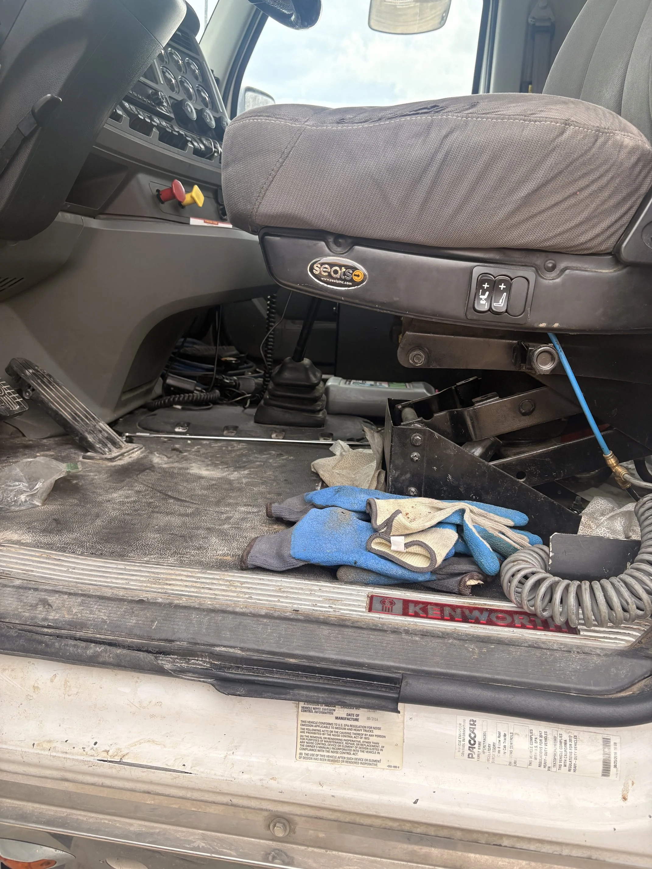 The interior of a vehicle showing a driver's seat with tools, paperwork, socks, and miscellaneous items on the floor and dashboard area.