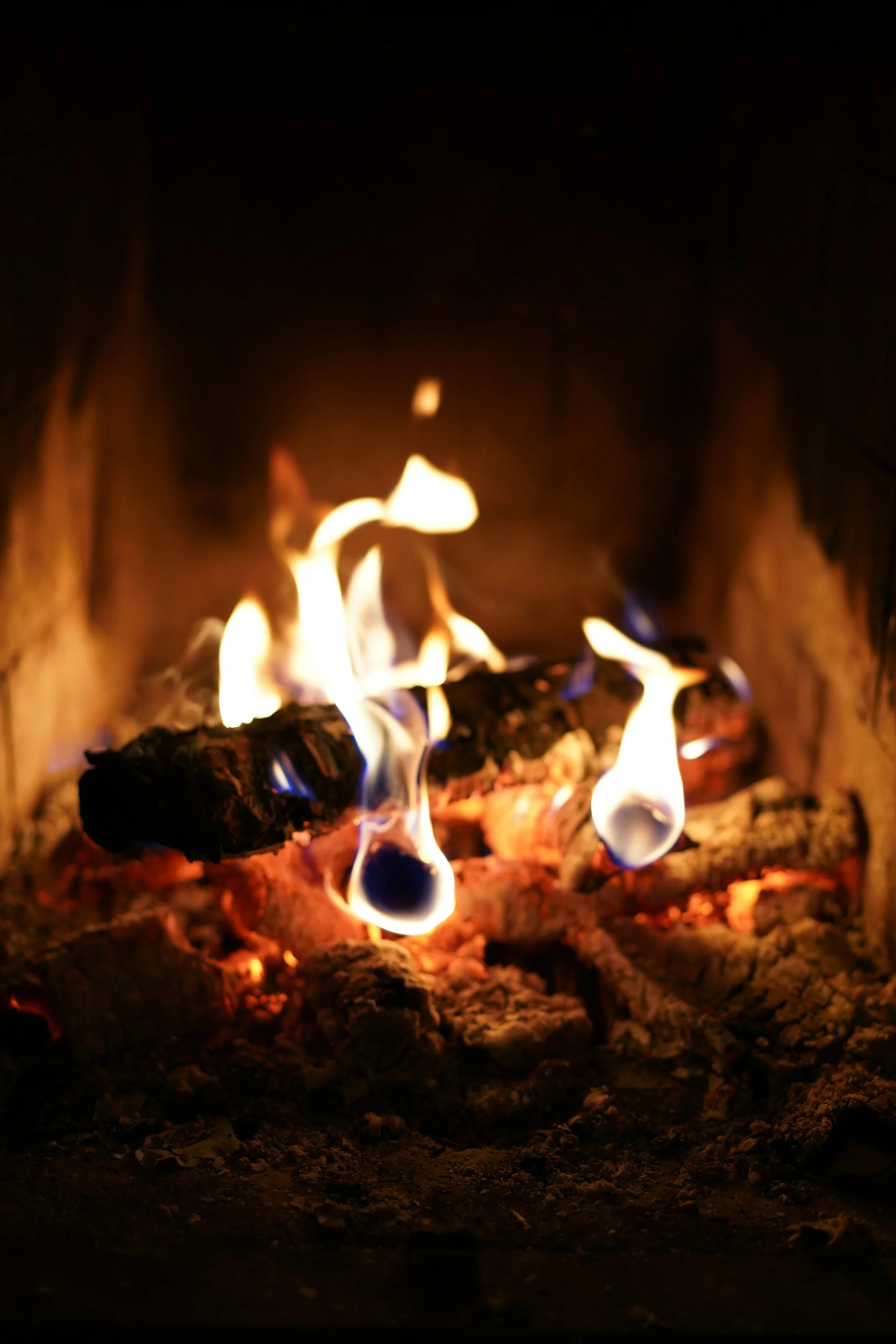 Close-up of glowing flames and burning wood inside a fire pit or fireplace with dark surroundings.