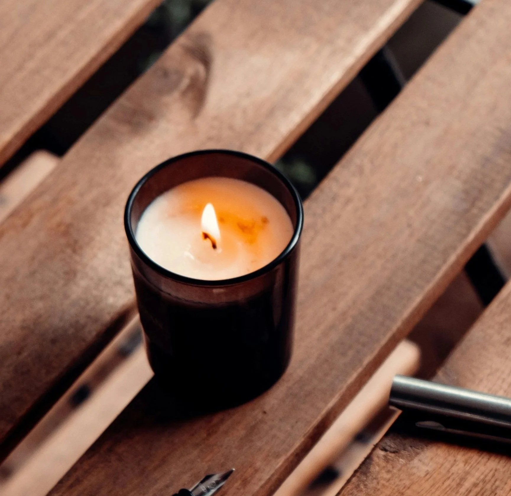 A lit candle with a black container on a wooden surface.