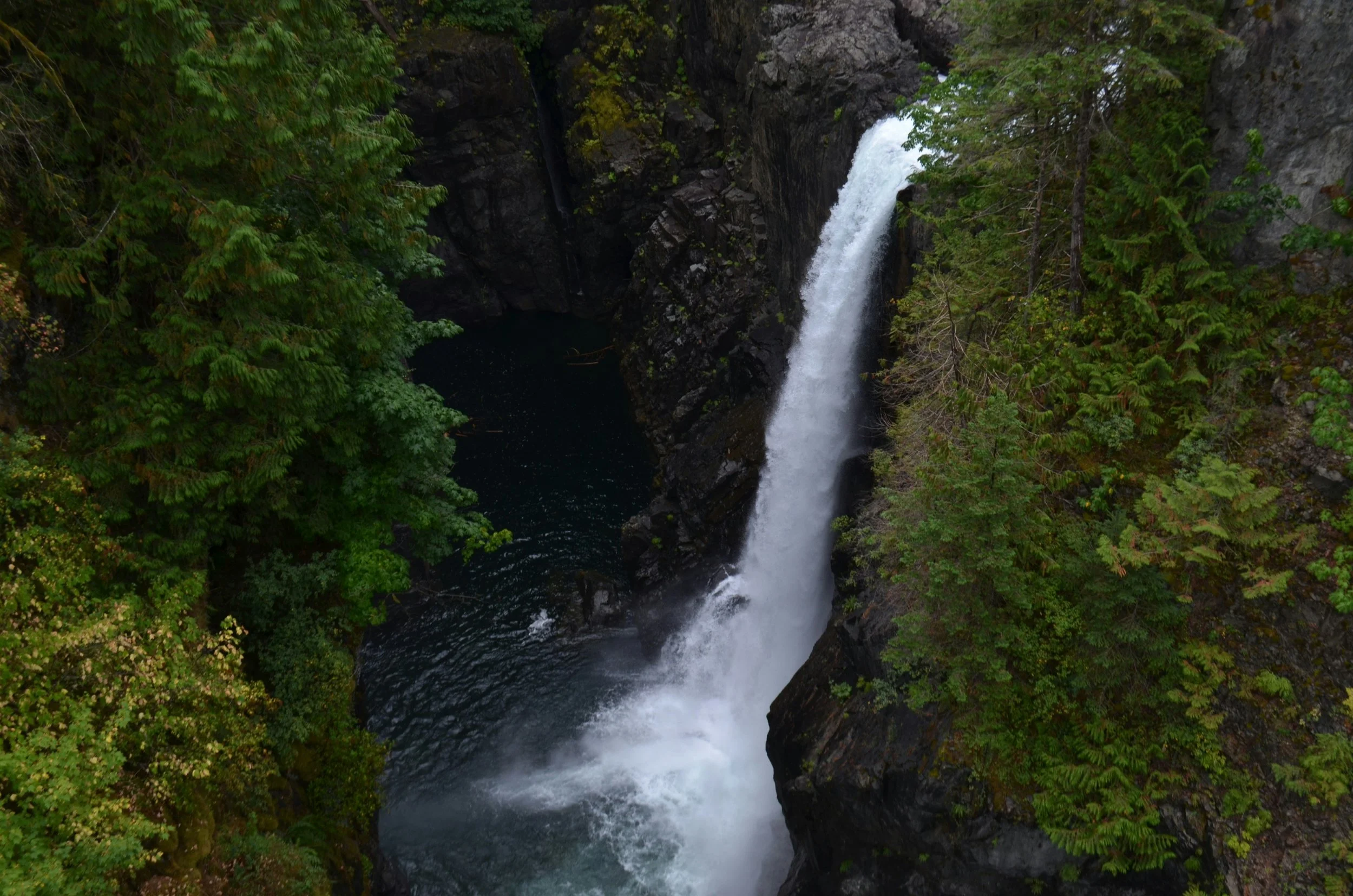 A waterfall flowing through a rocky canyon surrounded by dense green trees and foliage.