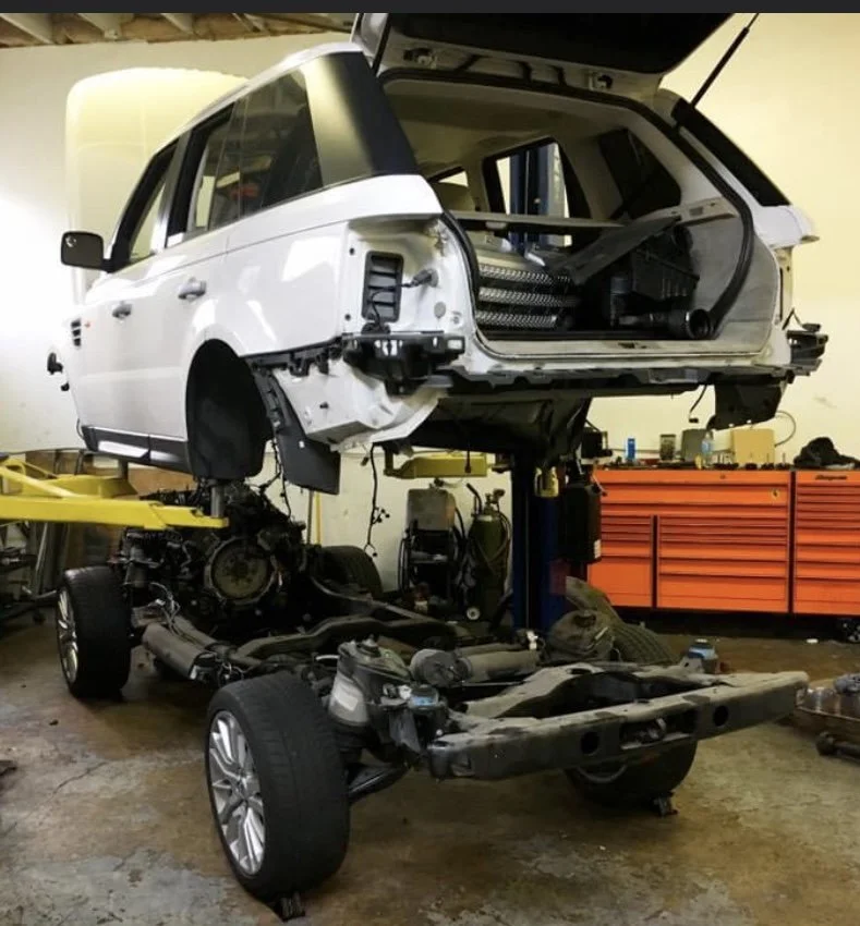 A partially disassembled white Range Rover SUV with the body lifted off the chassis in an auto repair shop.