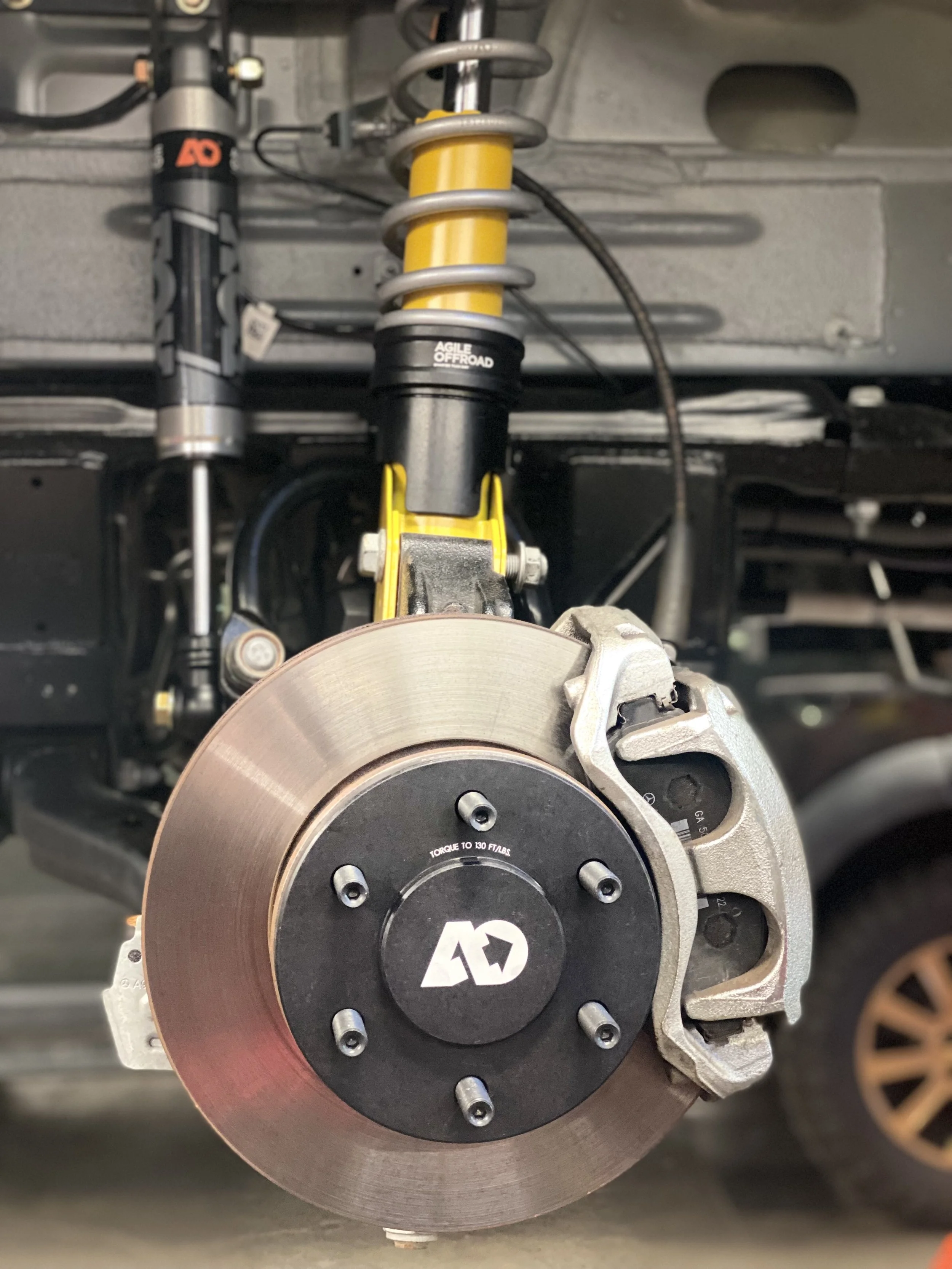 Close-up view of a yellow and black Agile Offroad brake disc and suspension setup, with a coil spring, brake caliper, and other suspension components visible.