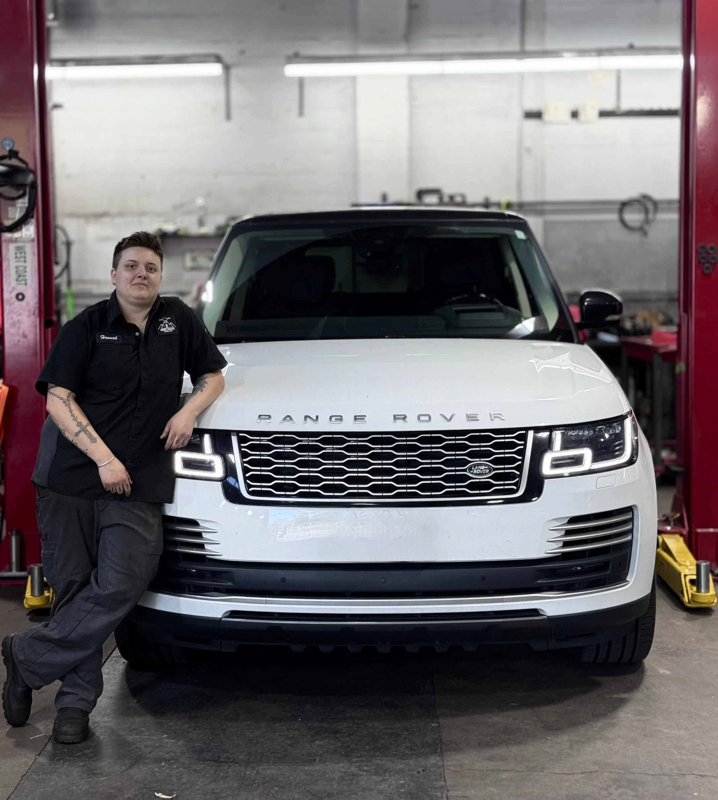 A Land Rover mechanic stands beside a white Range Rover in an auto repair shop.