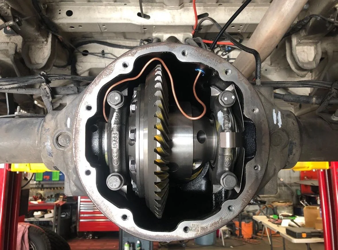 A close-up view of a differential inside a vehicle's axle housing, with visible gears and mechanical components, in a garage workshop setting.