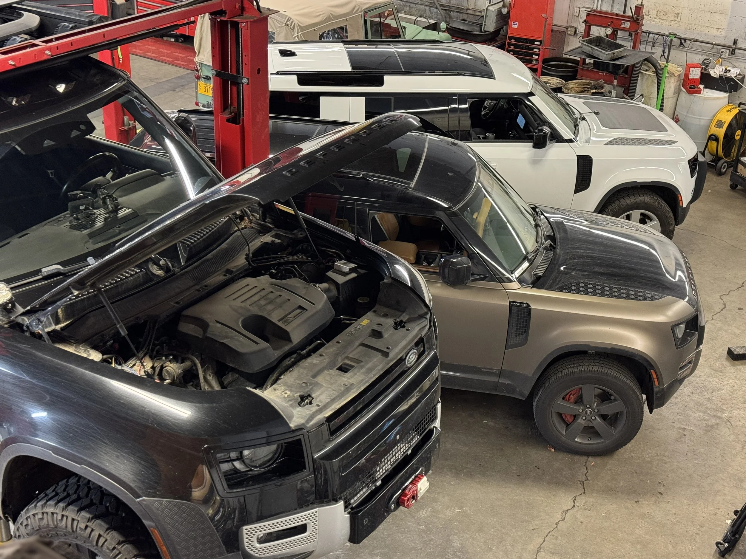 A garage filled with Land Rover Defenders, some of which have their hoods open, and tools and equipment in the background.