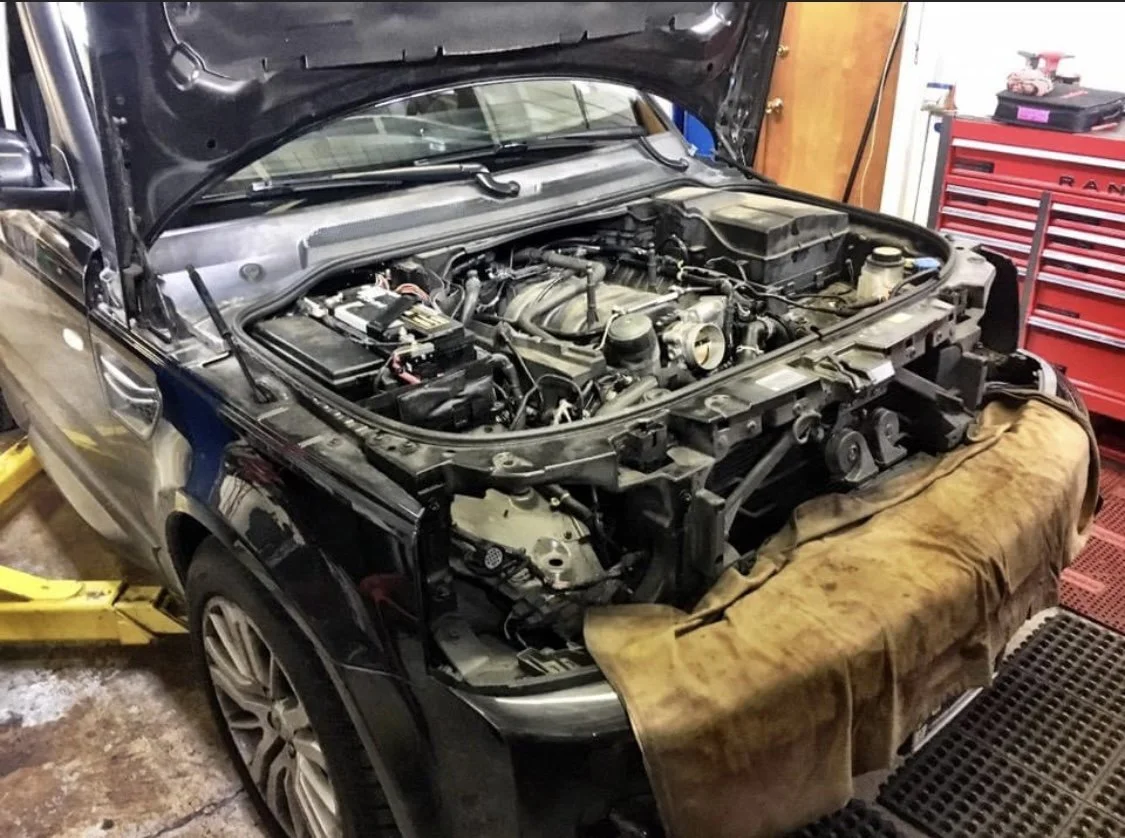 A black Land Rover with its hood open in a garage, showing an engine undergoing repair or maintenance, with a brown cloth covering part of the front.