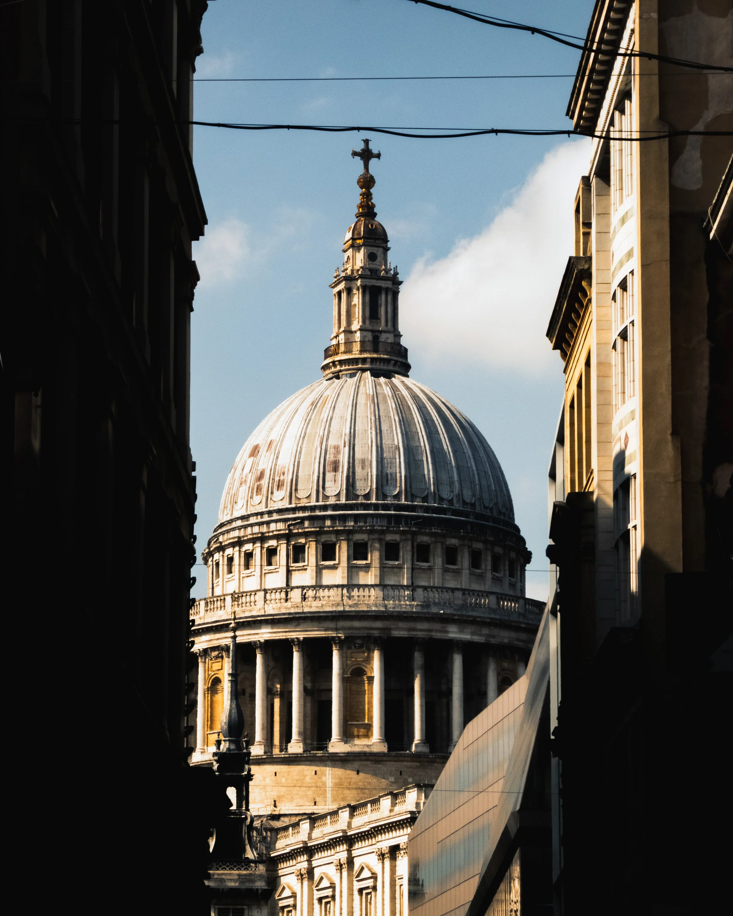 The dome of St. Paul's Cathedral seen between two buildings, with a cross on top of the dome and electrical wires crossing in the sky.