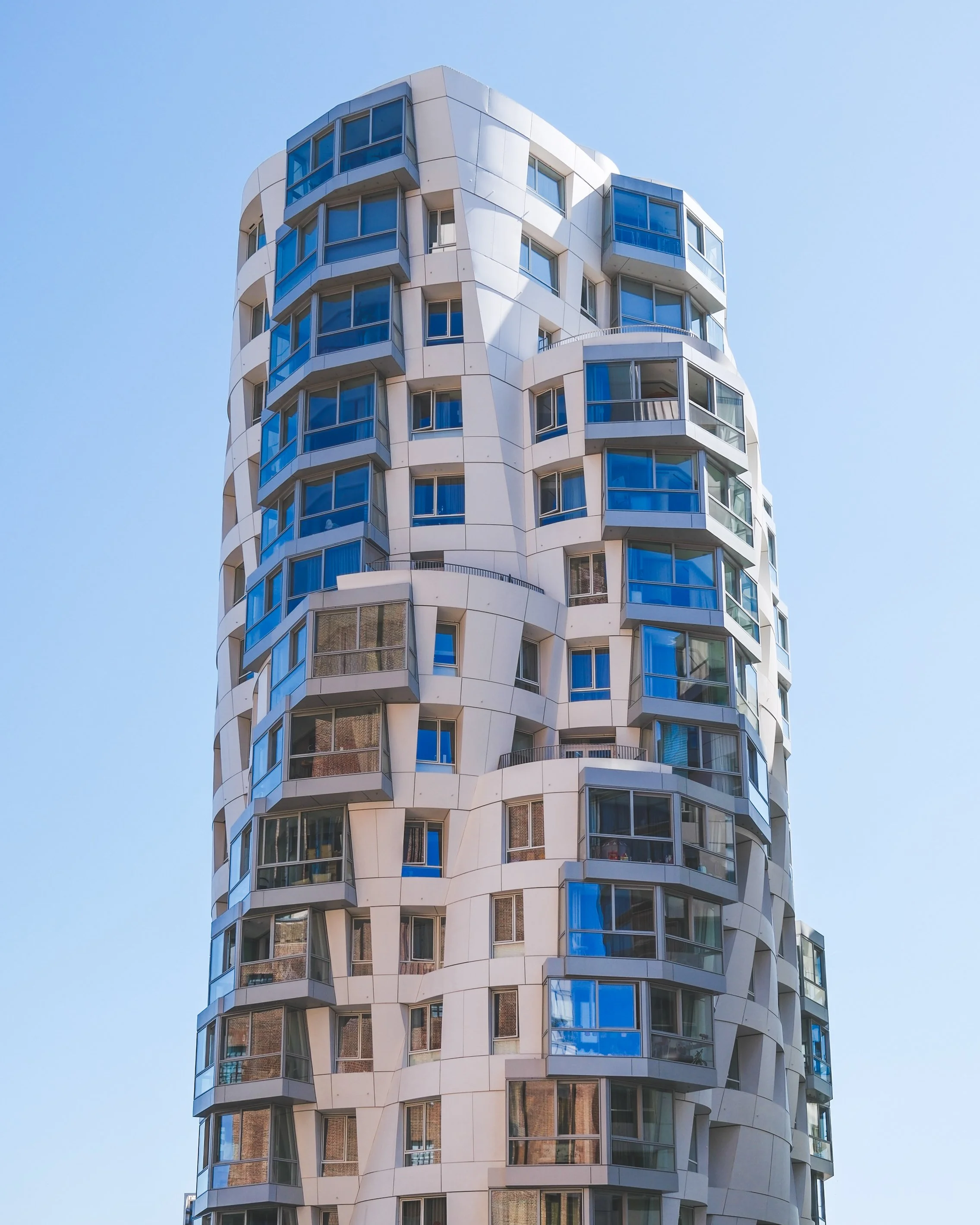 A modern high-rise building with rounded, irregularly shaped windows and etched white panels, set against a clear blue sky.