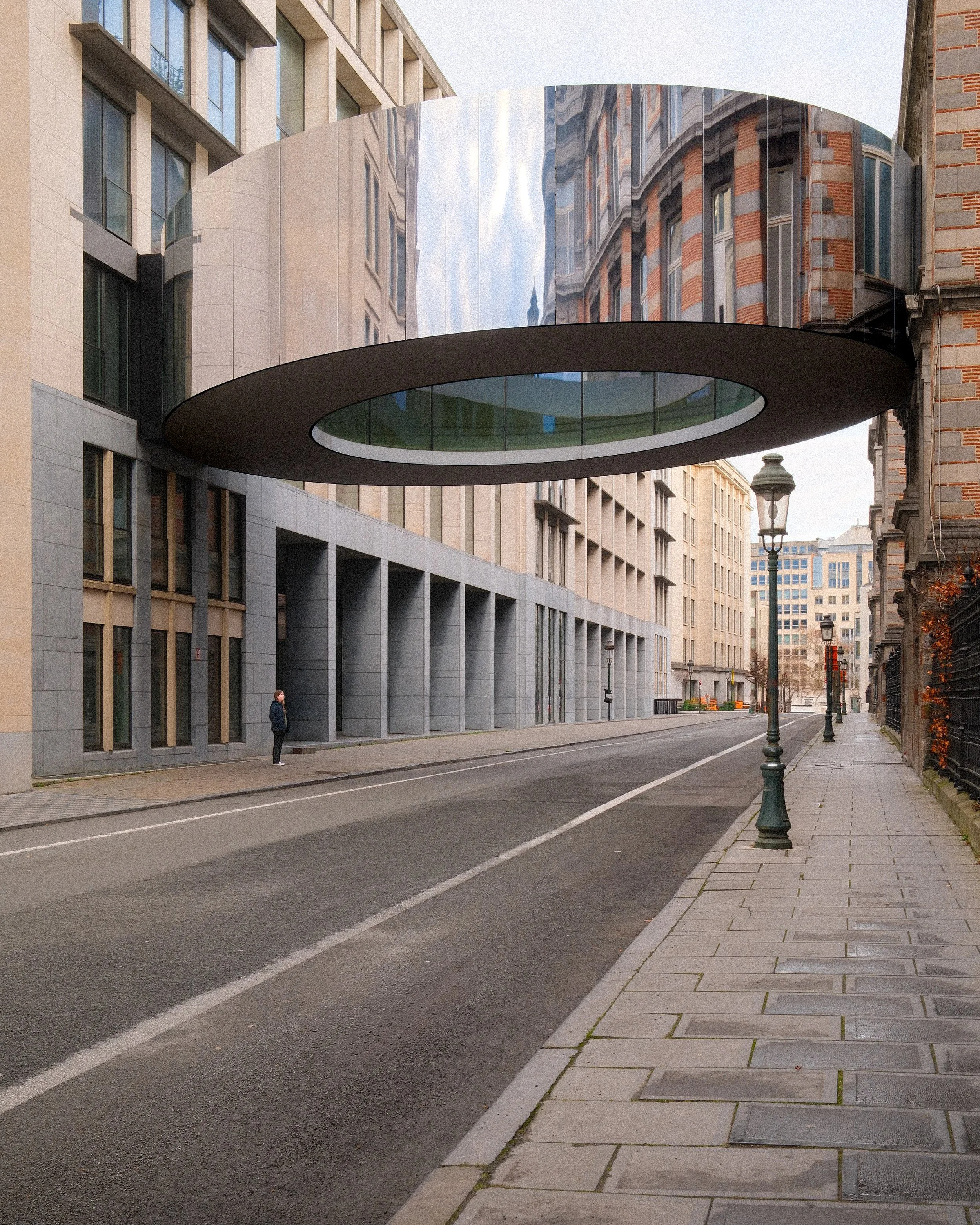 An urban street scene featuring modern buildings, a streetlamp, and a prominent floating spherical structure with mirrored and matte surfaces suspended above the sidewalk.