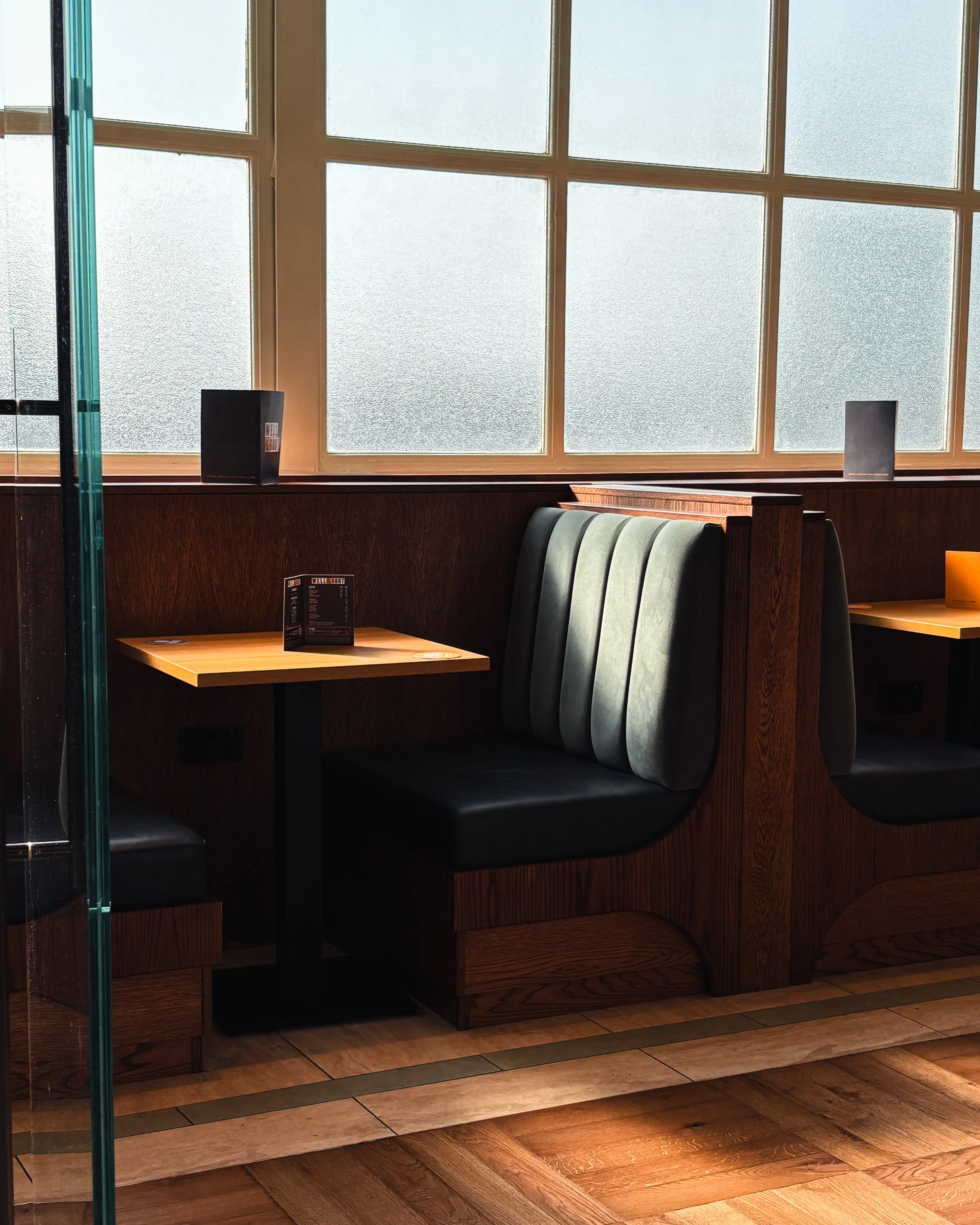 Interior of a cafe or restaurant with wooden booths, frosted windows, menus on the table, and a hardwood floor.