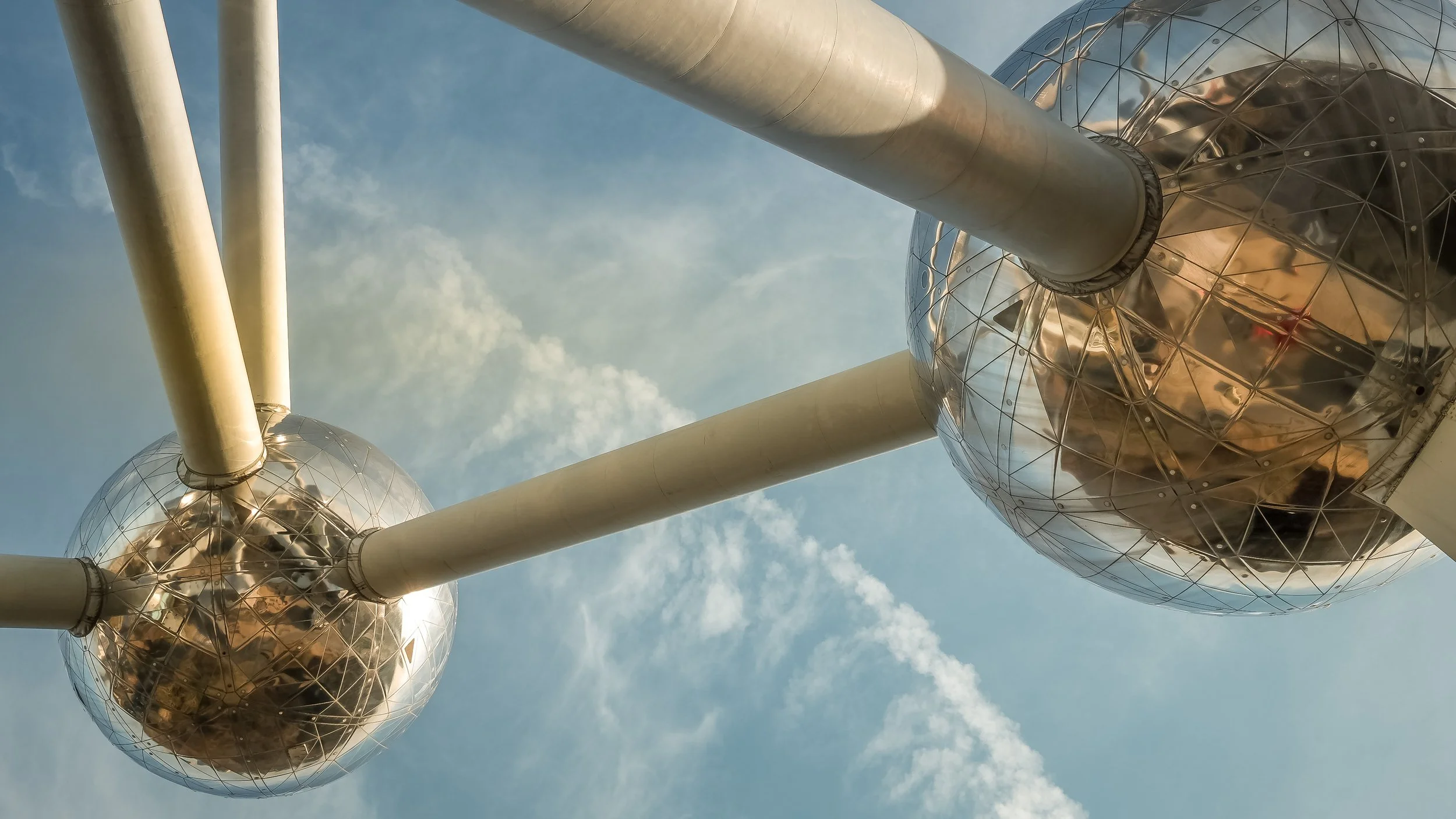 Close-up of the Atomium structure in Brussels, Belgium, showing metallic spheres connected by tubes, set against a partly cloudy sky.