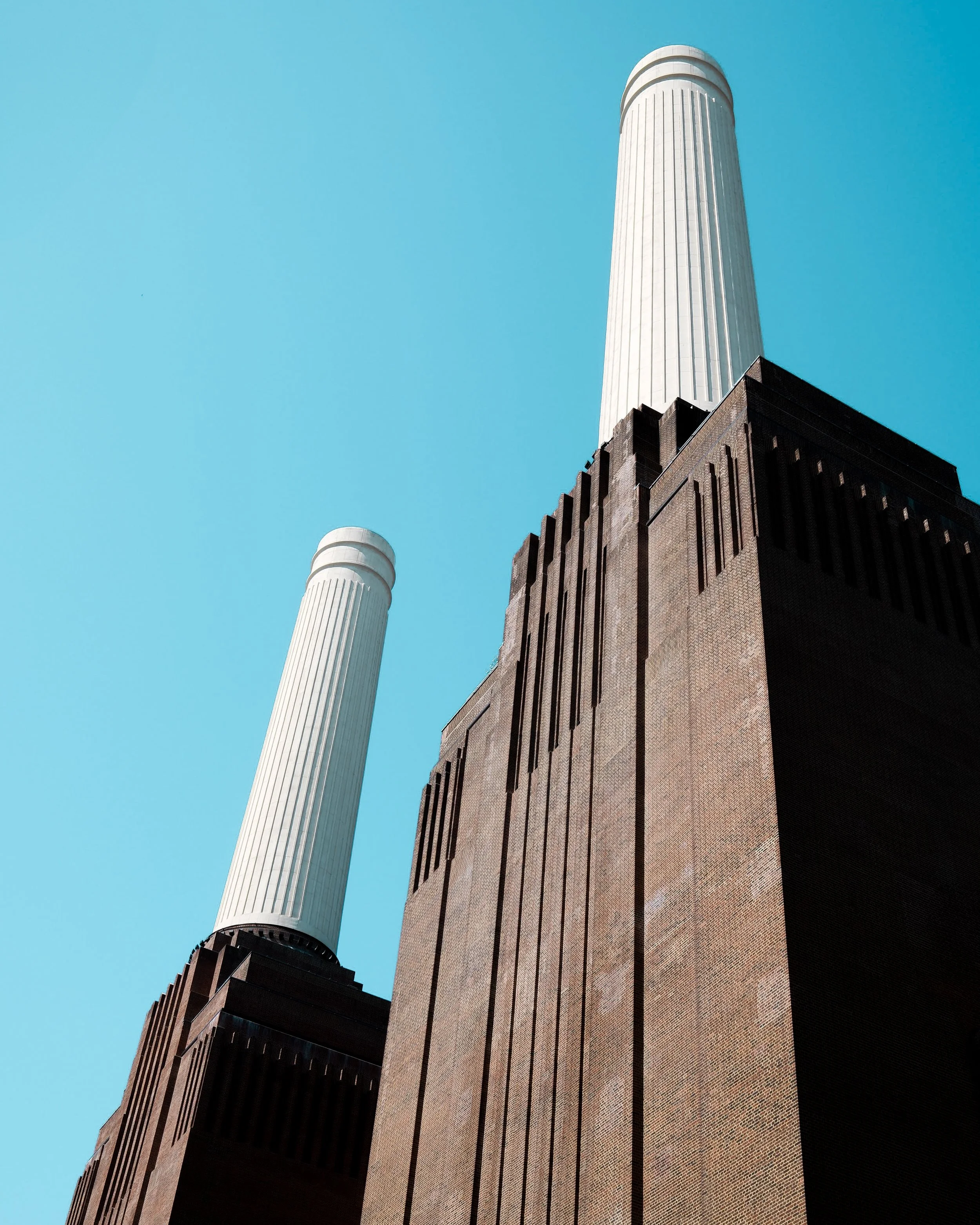A tall modern building with a brick facade and vertical lines next to a white cylindrical tower with a rounded top, against a bright blue sky.